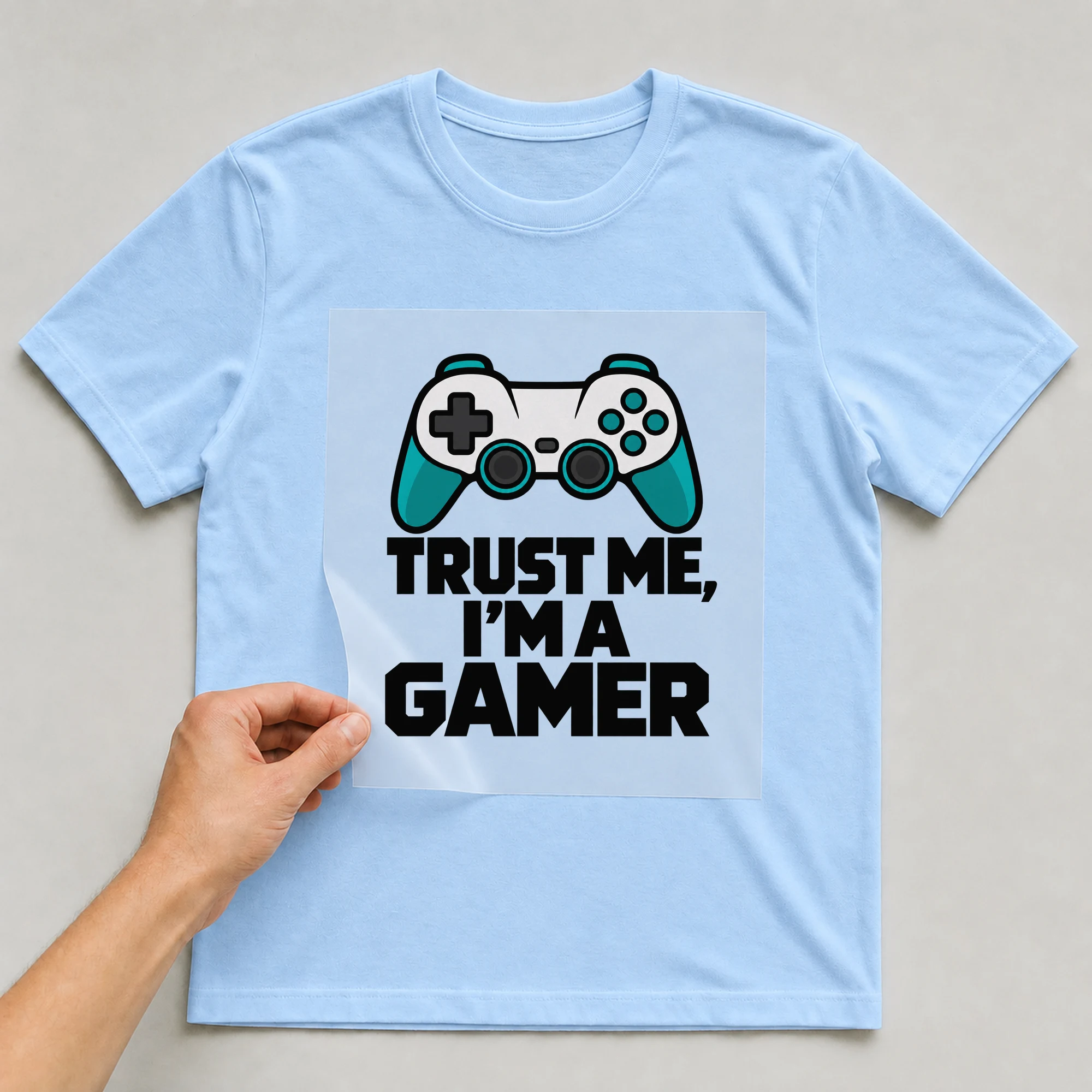 Bügelbild „Trust Me, I'm A Gamer“ auf babyblauem T-Shirt, Folie wird aufgelegt