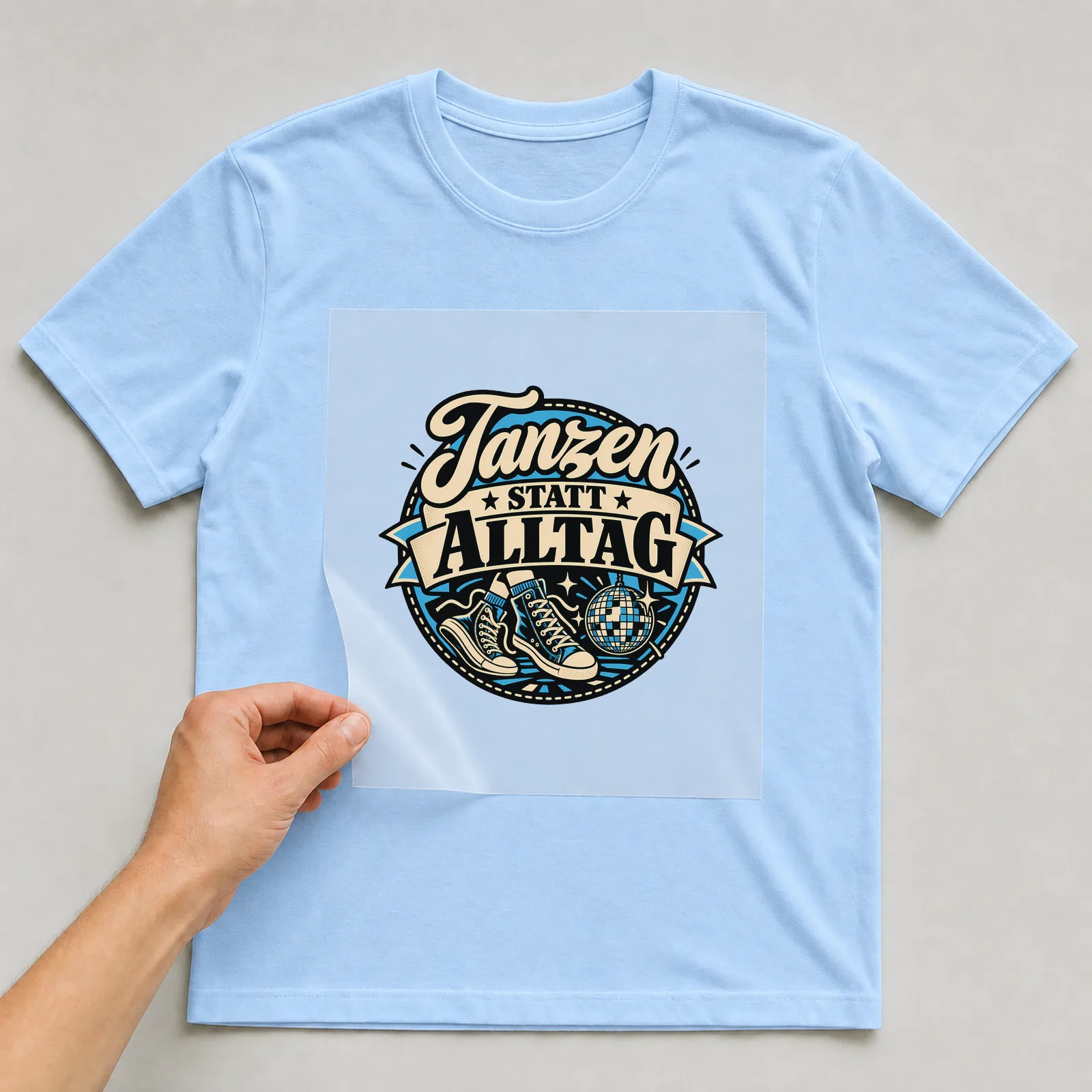 Bügelbild „Tanzen statt Alltag“ auf hellblauem T-Shirt, Folie wird aufgelegt