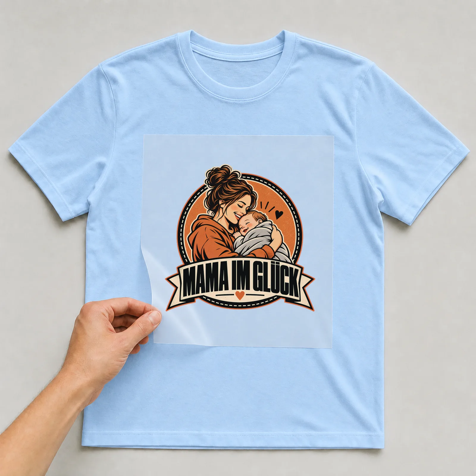 Bügelbild „Mama im Glück“ auf hellblauem T-Shirt, Folie wird aufgelegt
