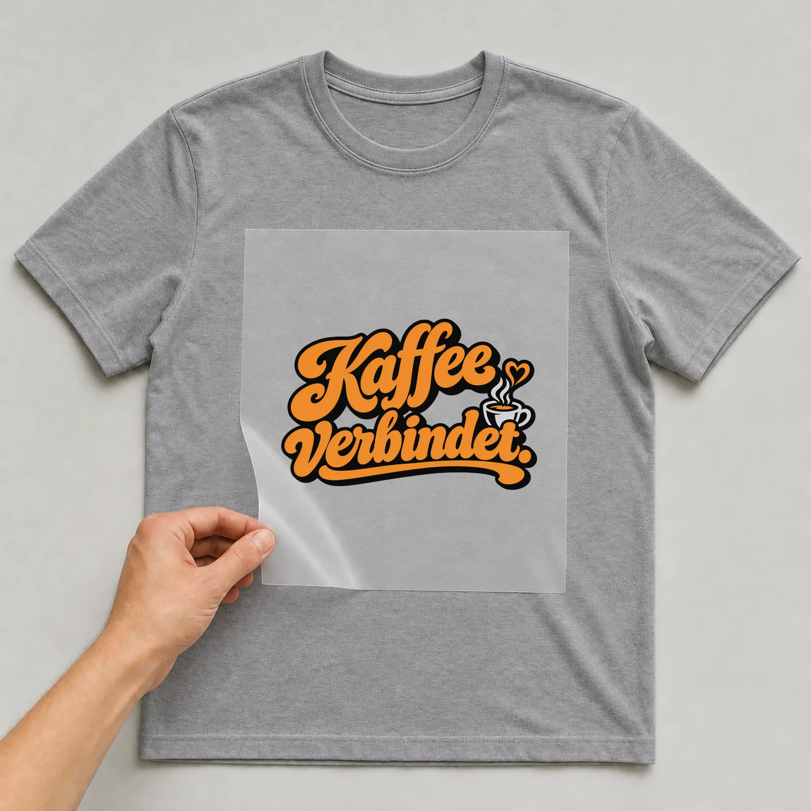 Bügelbild „Kaffee verbindet“ auf grauem T-Shirt, Folie wird aufgelegt
