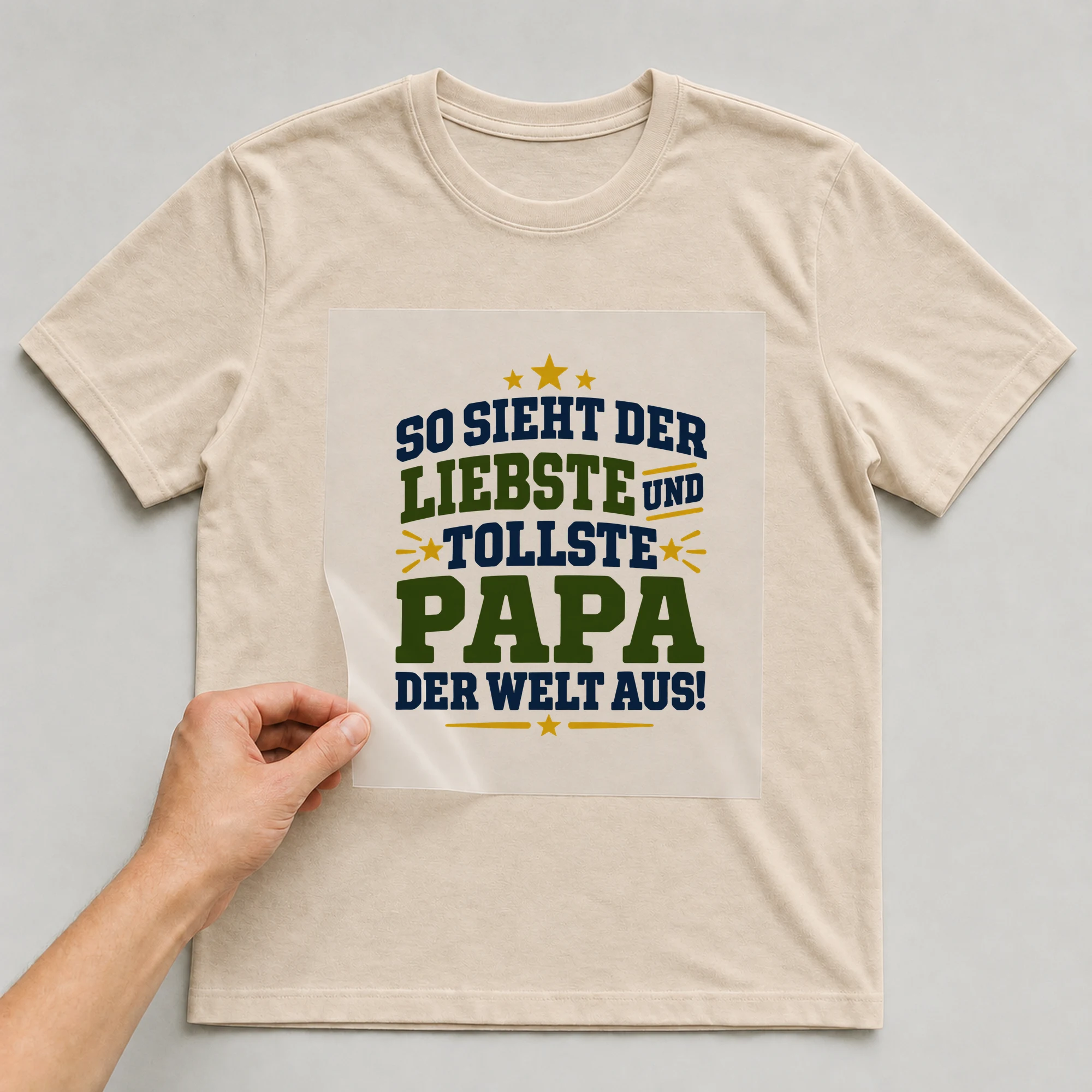 Bügelbild „So sieht der liebste und tollste Papa der Welt aus!“ auf beigem T-Shirt, Folie wird aufgelegt