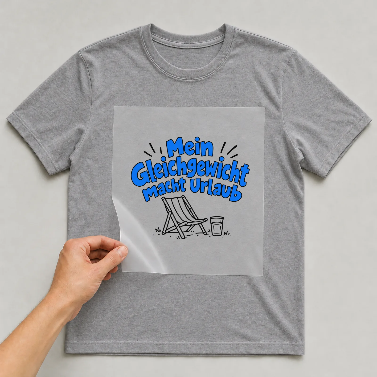 Bügelbild „Mein Gleichgewicht macht Urlaub“ auf grauem T-Shirt, Folie wird aufgelegt
