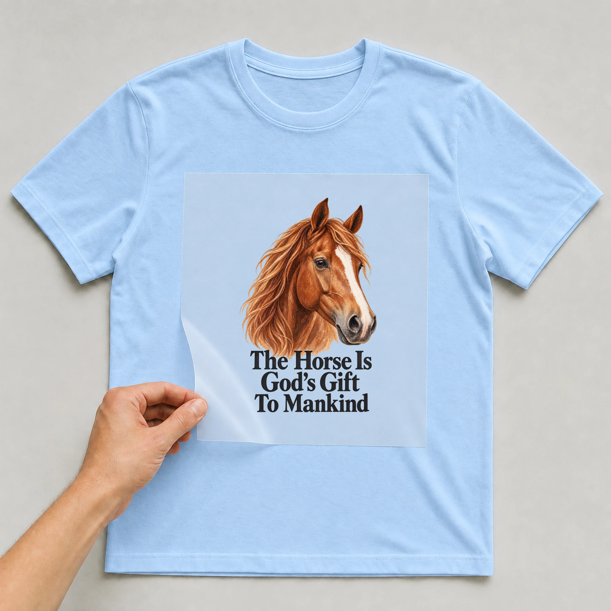 Bügelbild „The Horse Is God's Gift To Mankind“ auf babyblauem T-Shirt, Folie wird aufgelegt