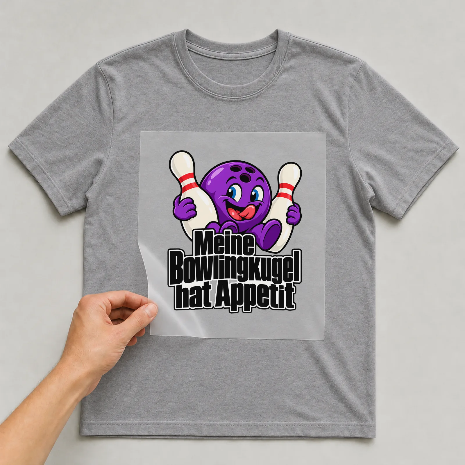 Bügelbild „Meine Bowlingkugel hat Appetit“ auf grauem T-Shirt, Folie wird aufgelegt