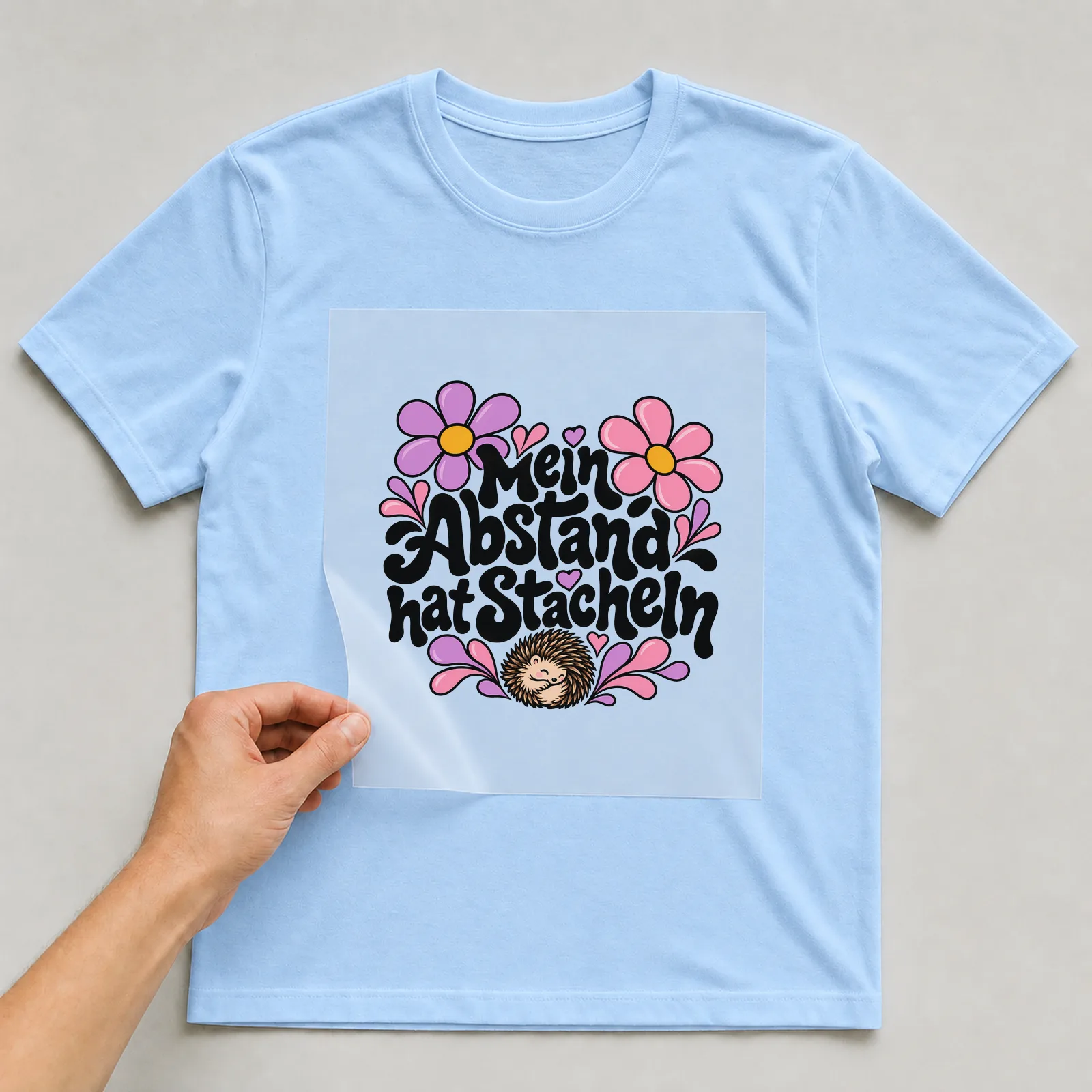 Bügelbild „Mein Abstand hat Stacheln“ auf hellblauem T-Shirt, Folie wird aufgelegt