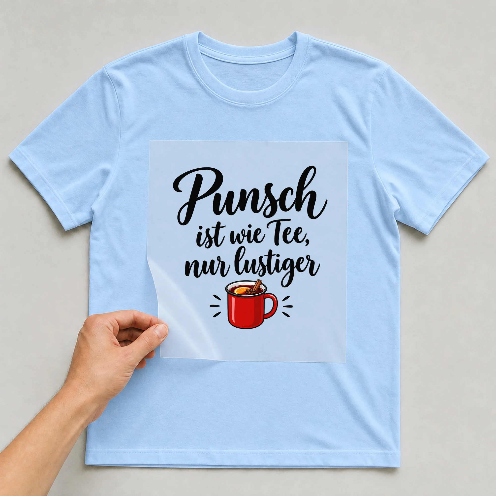 Bügelbild „Punsch ist wie Tee, nur lustiger“ auf babyblauem T-Shirt, Folie wird aufgelegt