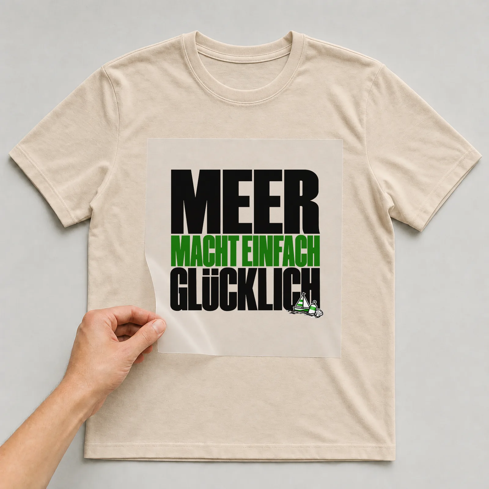 Bügelbild „Meer macht einfach glücklich“ auf beigem T-Shirt, Folie wird aufgelegt