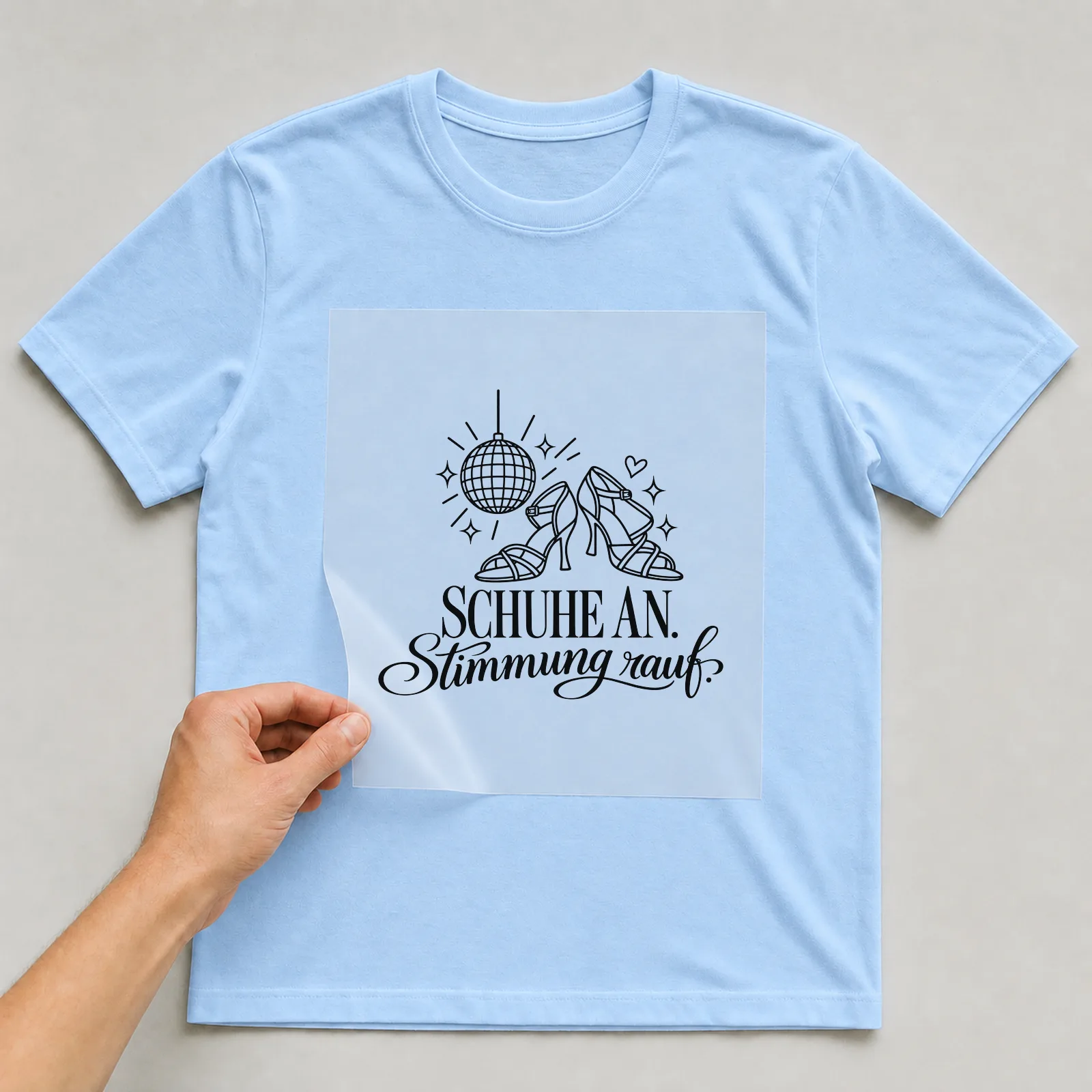 Bügelbild „Schuhe an. Stimmung rauf.“ auf hellblauem T-Shirt, Folie wird aufgelegt