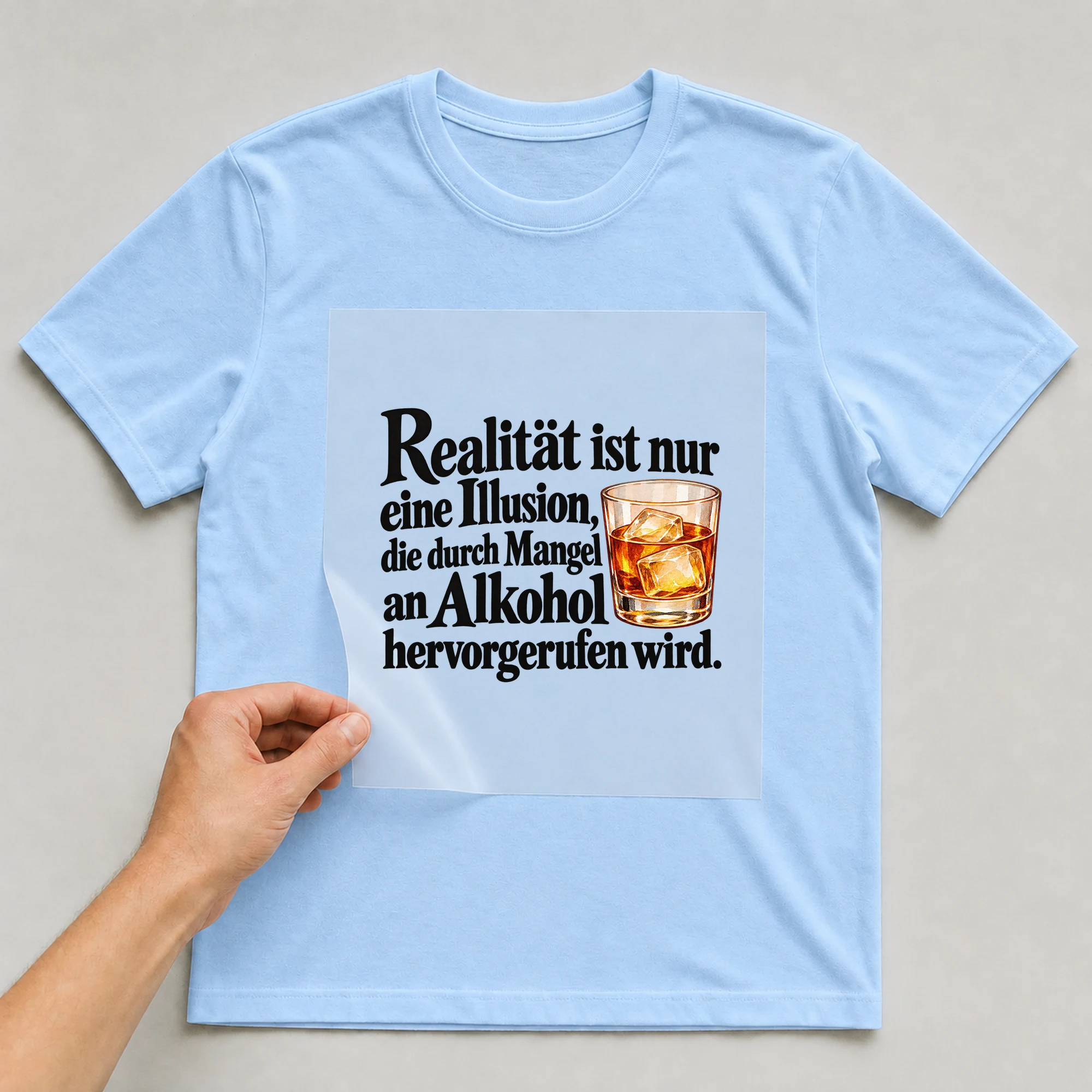 Bügelbild „Realität ist nur eine Illusion, die durch Mangel an Alkohol hervorgerufen“ auf babyblauem T-Shirt, Folie wird aufgelegt