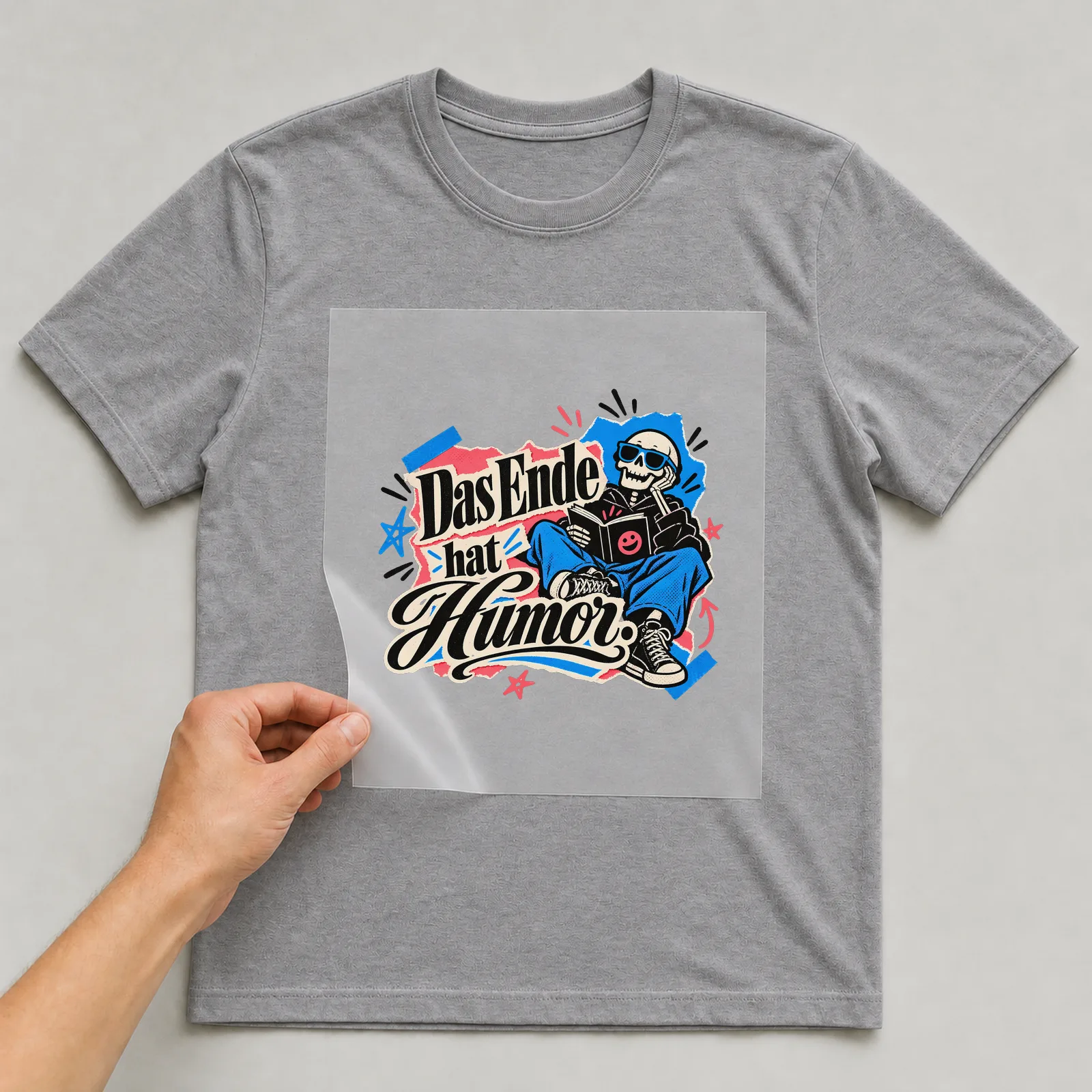 Bügelbild „Das Ende hat Humor“ auf grauem T-Shirt, Folie wird aufgelegt