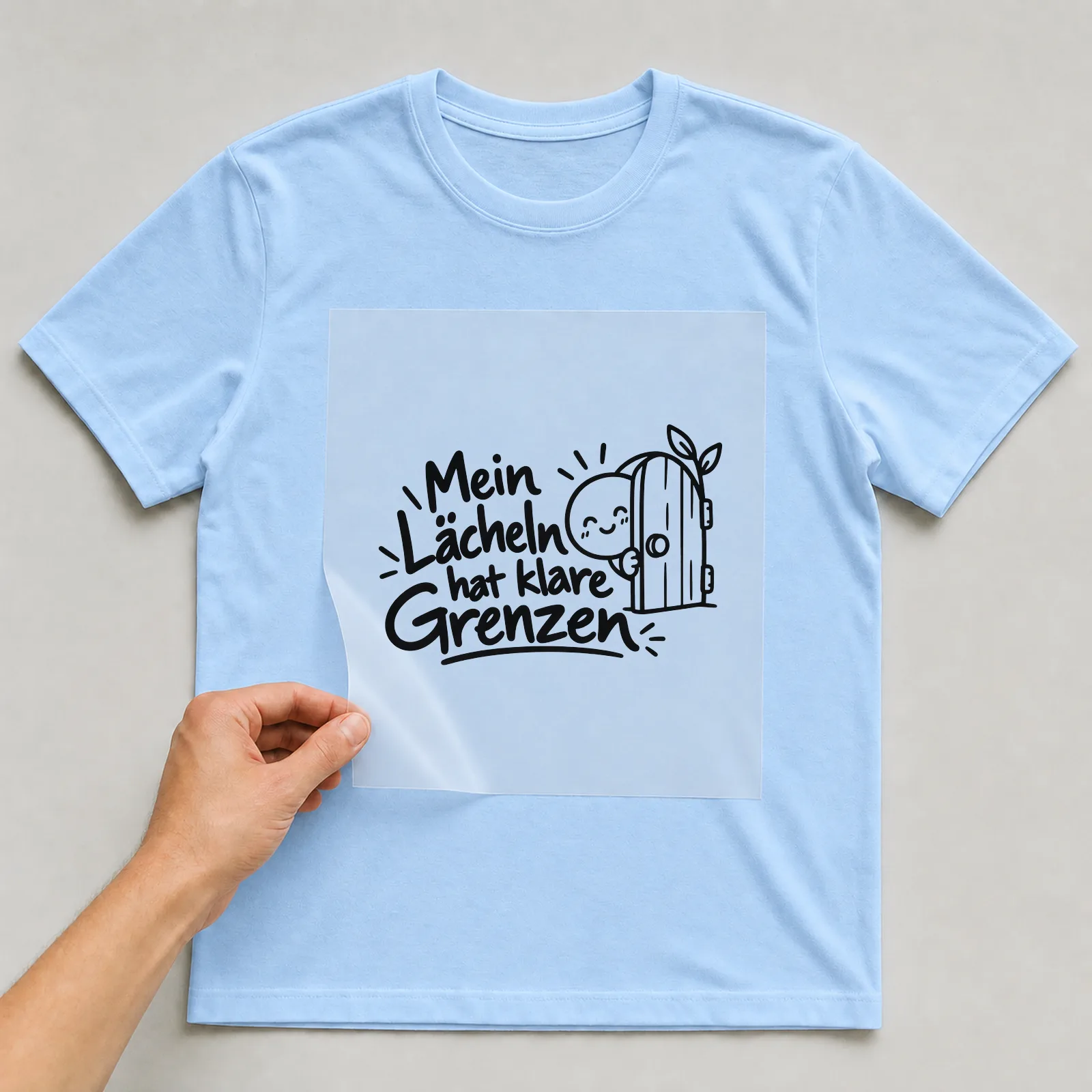 Bügelbild „Mein Lächeln hat klare Grenzen“ auf hellblauem T-Shirt, Folie wird aufgelegt