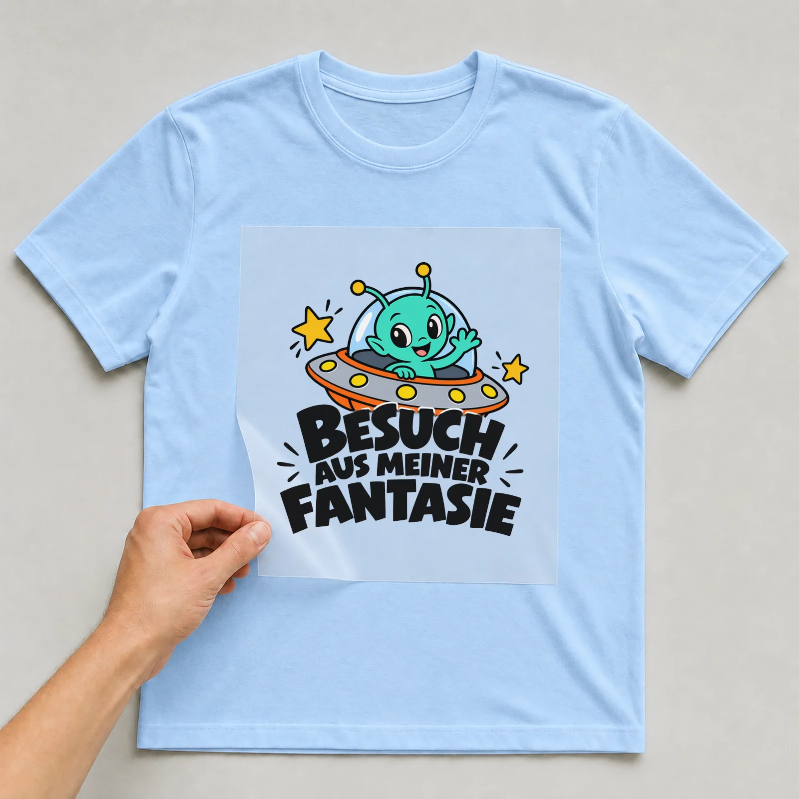 Bügelbild „Besuch aus meiner Fantasie“ auf hellblauem T-Shirt, Folie wird aufgelegt