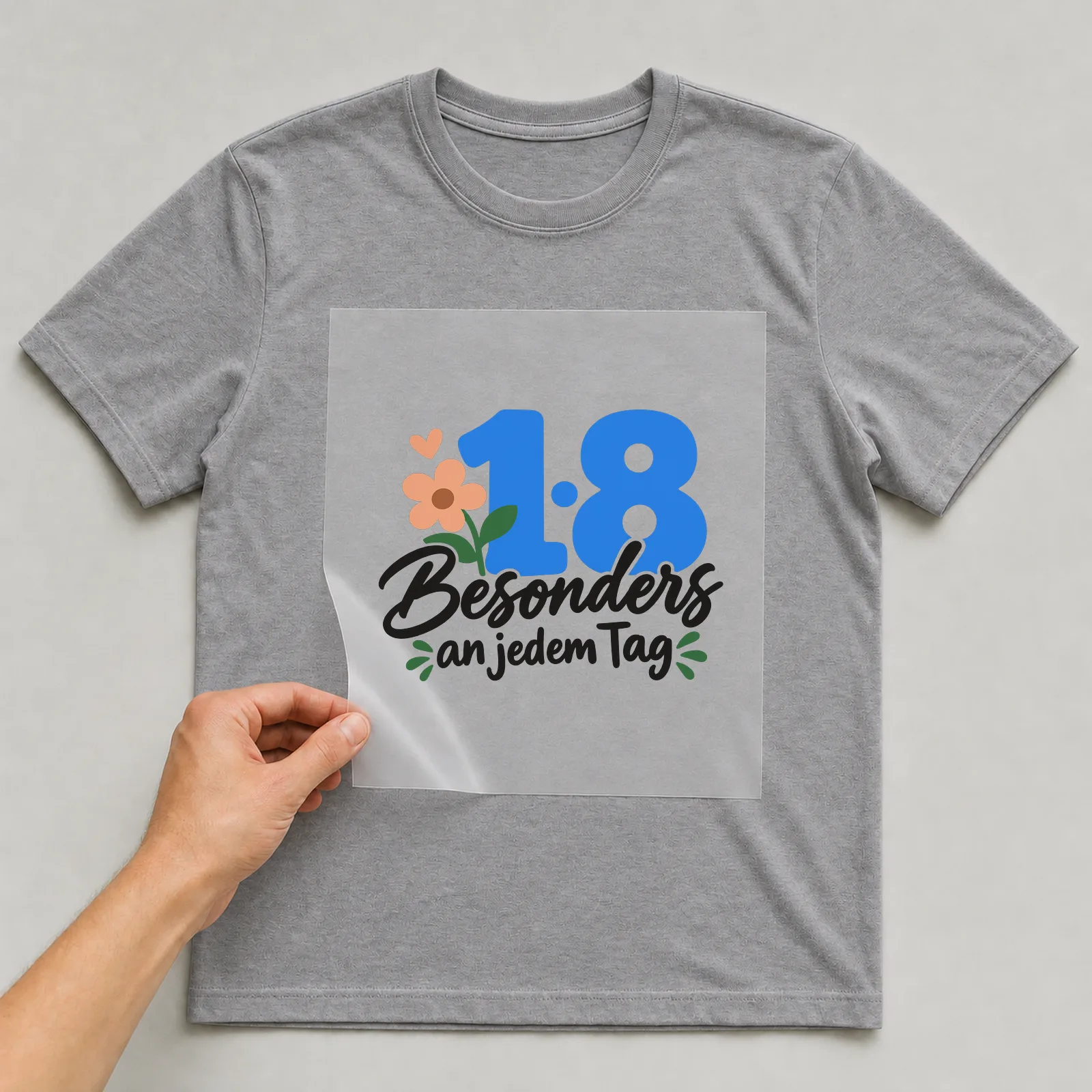 Bügelbild „18 · Besonders an jedem Tag“ auf grauem T-Shirt, Folie wird aufgelegt