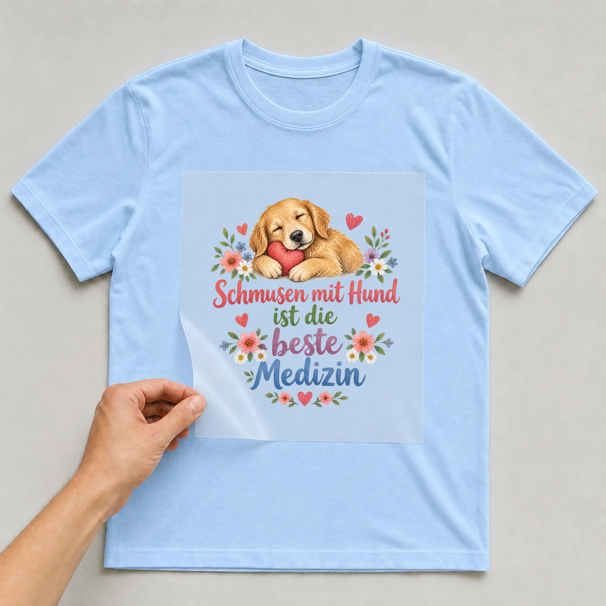 Bügelbild „Schmusen mit Hund ist die beste Medizin“ auf babyblauem T-Shirt, Folie wird aufgelegt