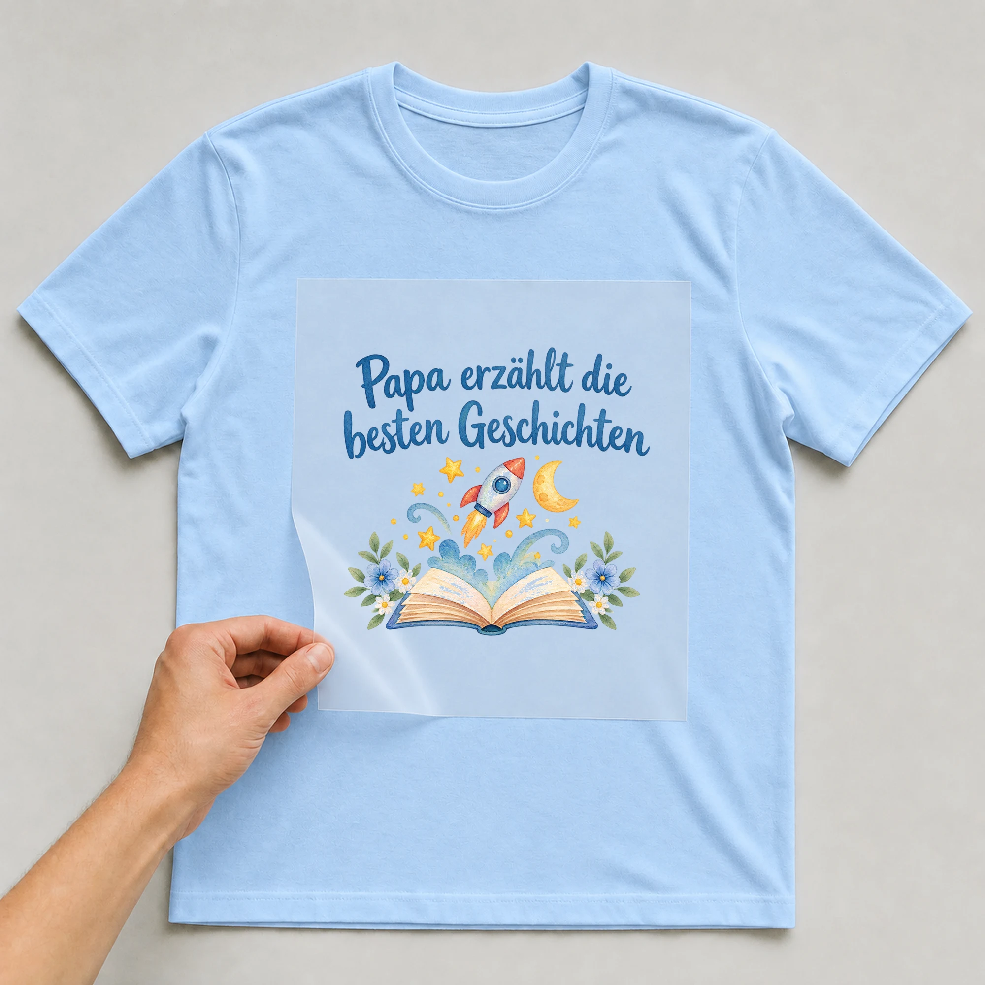Bügelbild „Papa erzählt die besten Geschichten“ auf babyblauem T-Shirt, Folie wird aufgelegt