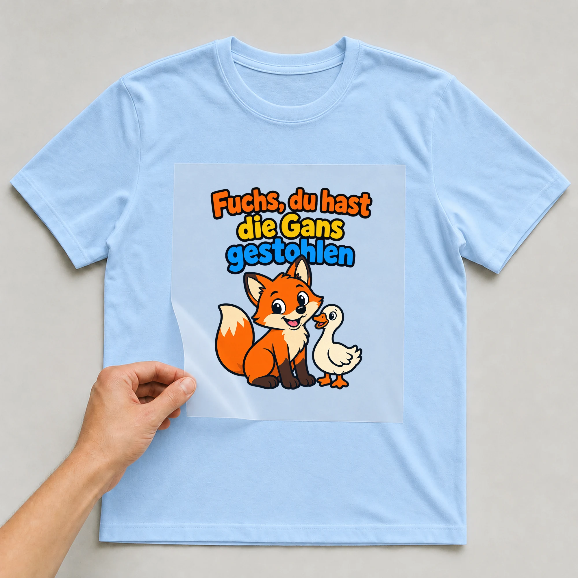 Bügelbild „Fuchs, du hast die Gans gestohlen“ auf babyblauem T-Shirt, Folie wird aufgelegt