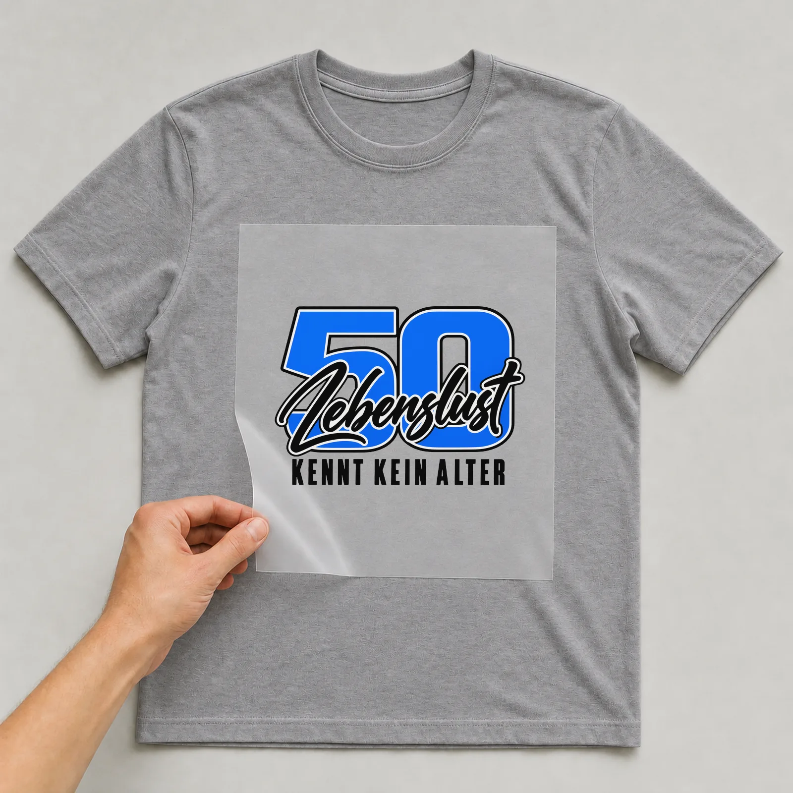 Bügelbild „50 · Lebenslust · Kennt kein Alter“ auf grauem T-Shirt, Folie wird aufgelegt