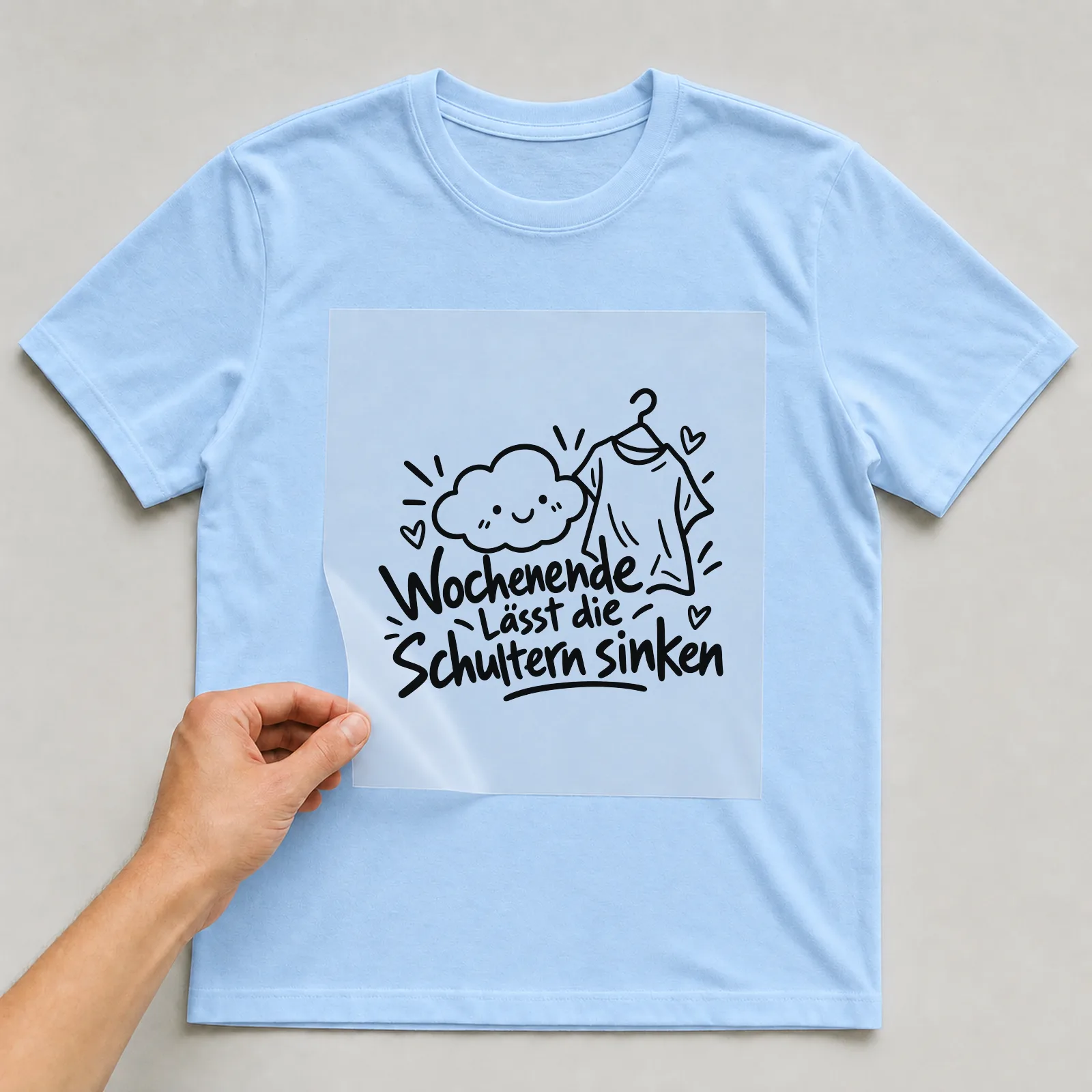 Bügelbild „Wochenende lässt die Schultern sinken“ auf hellblauem T-Shirt, Folie wird aufgelegt