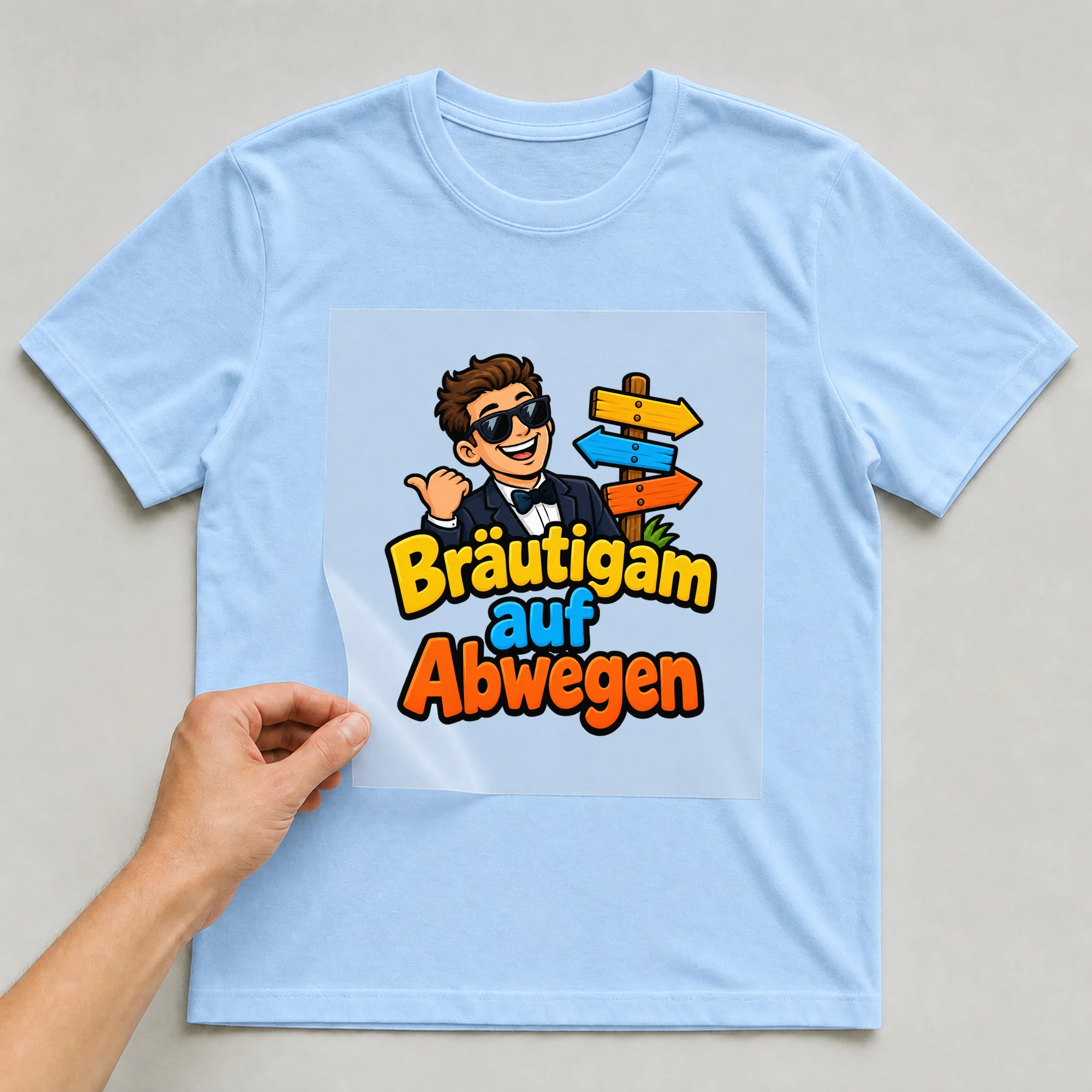 Bügelbild „Braeutigam auf abwegen“ auf babyblauem T-Shirt, Folie wird aufgelegt