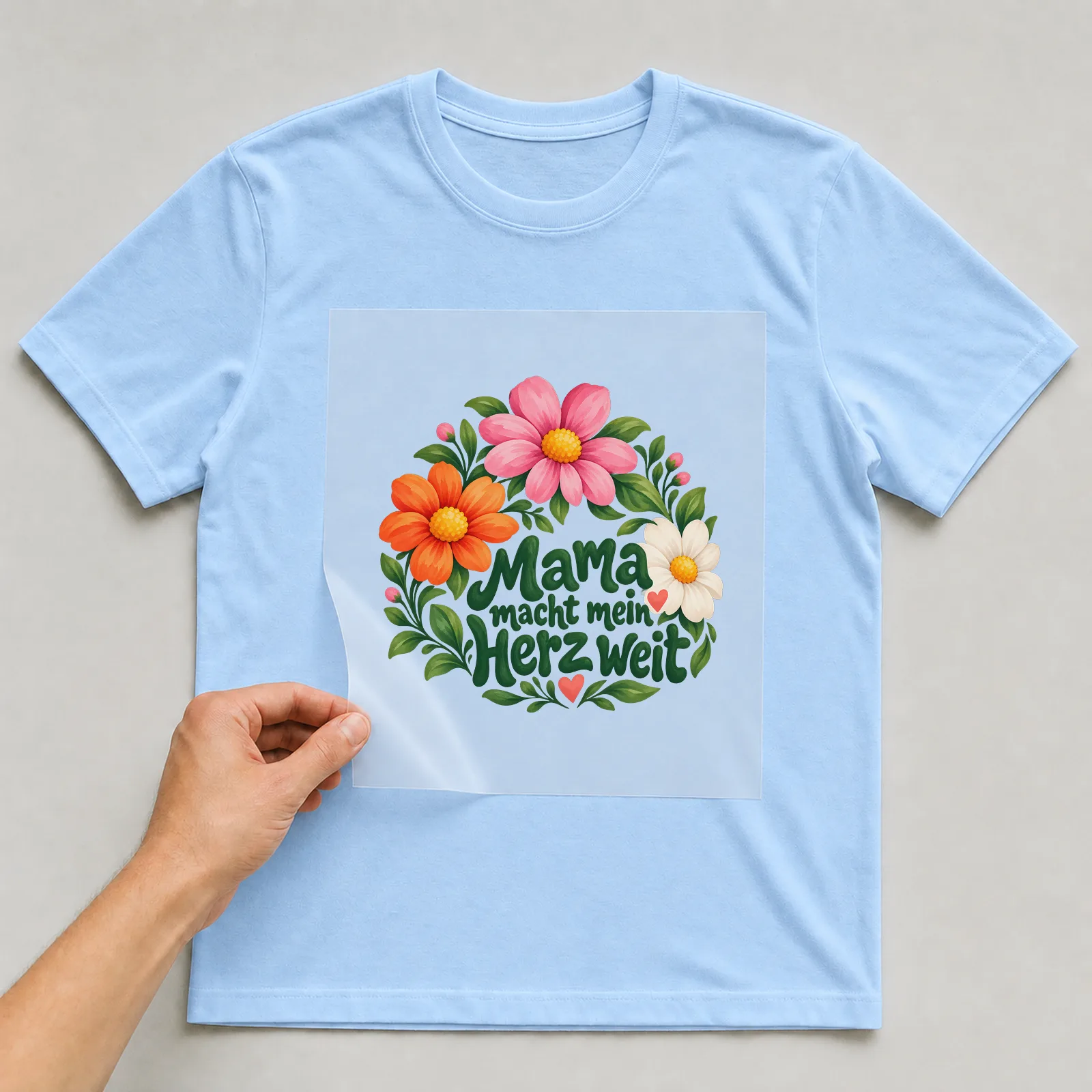Bügelbild „Mama macht mein Herz weit“ auf hellblauem T-Shirt, Folie wird aufgelegt