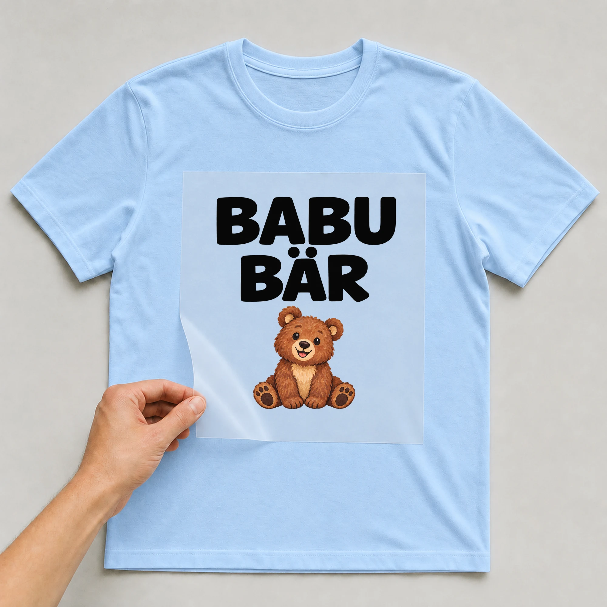 Bügelbild „BABU BÄR“ auf babyblauem T-Shirt, Folie wird aufgelegt