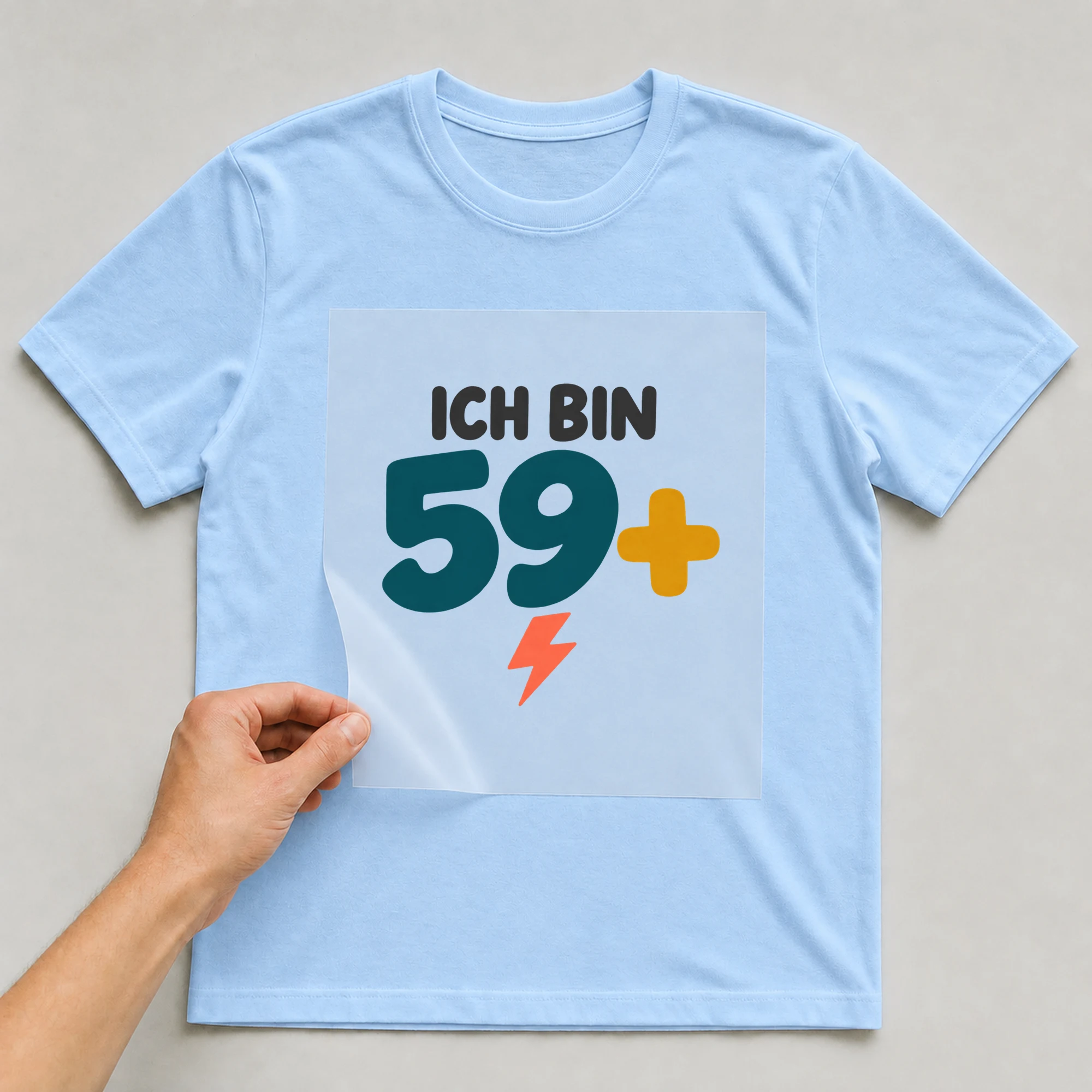 Bügelbild „Ich bin 59+“ auf babyblauem T-Shirt, Folie wird aufgelegt