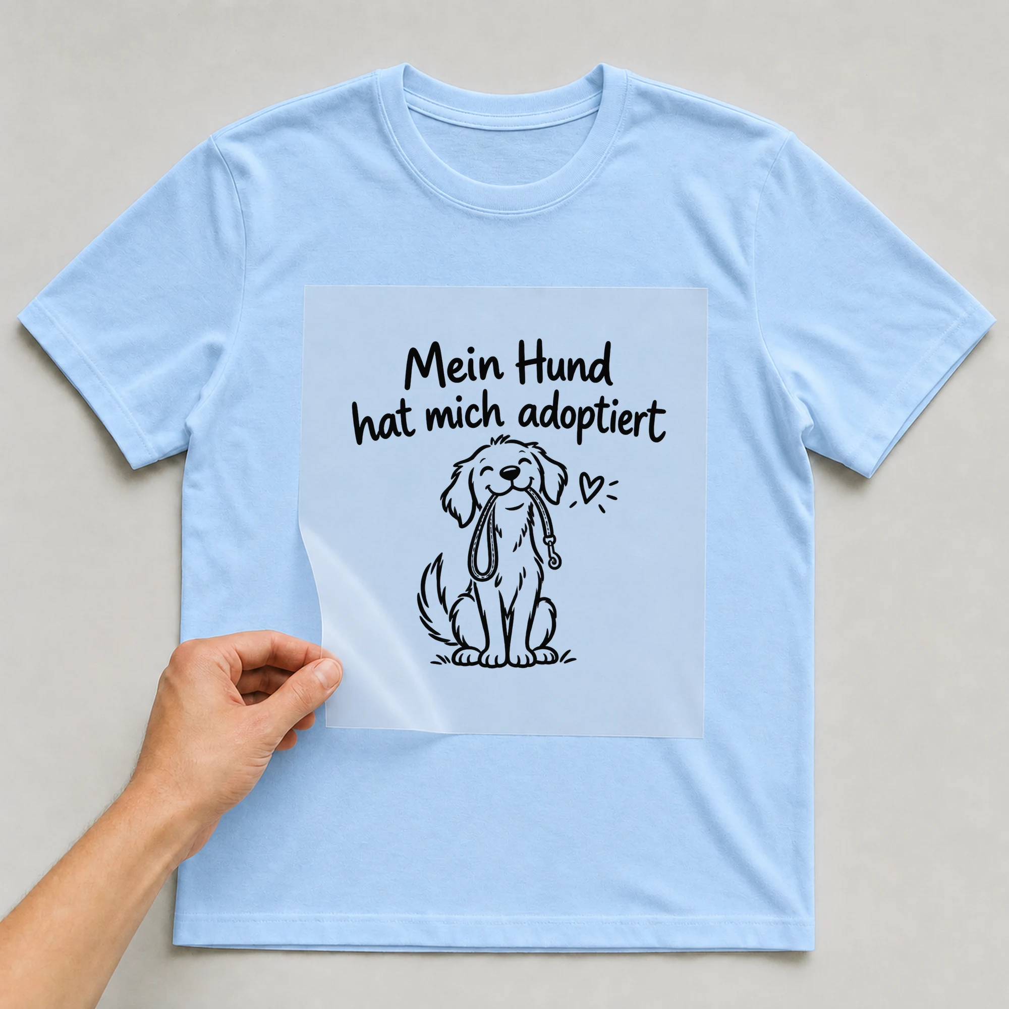 Bügelbild „Mein Hund hat mich adoptiert“ auf babyblauem T-Shirt, Folie wird aufgelegt