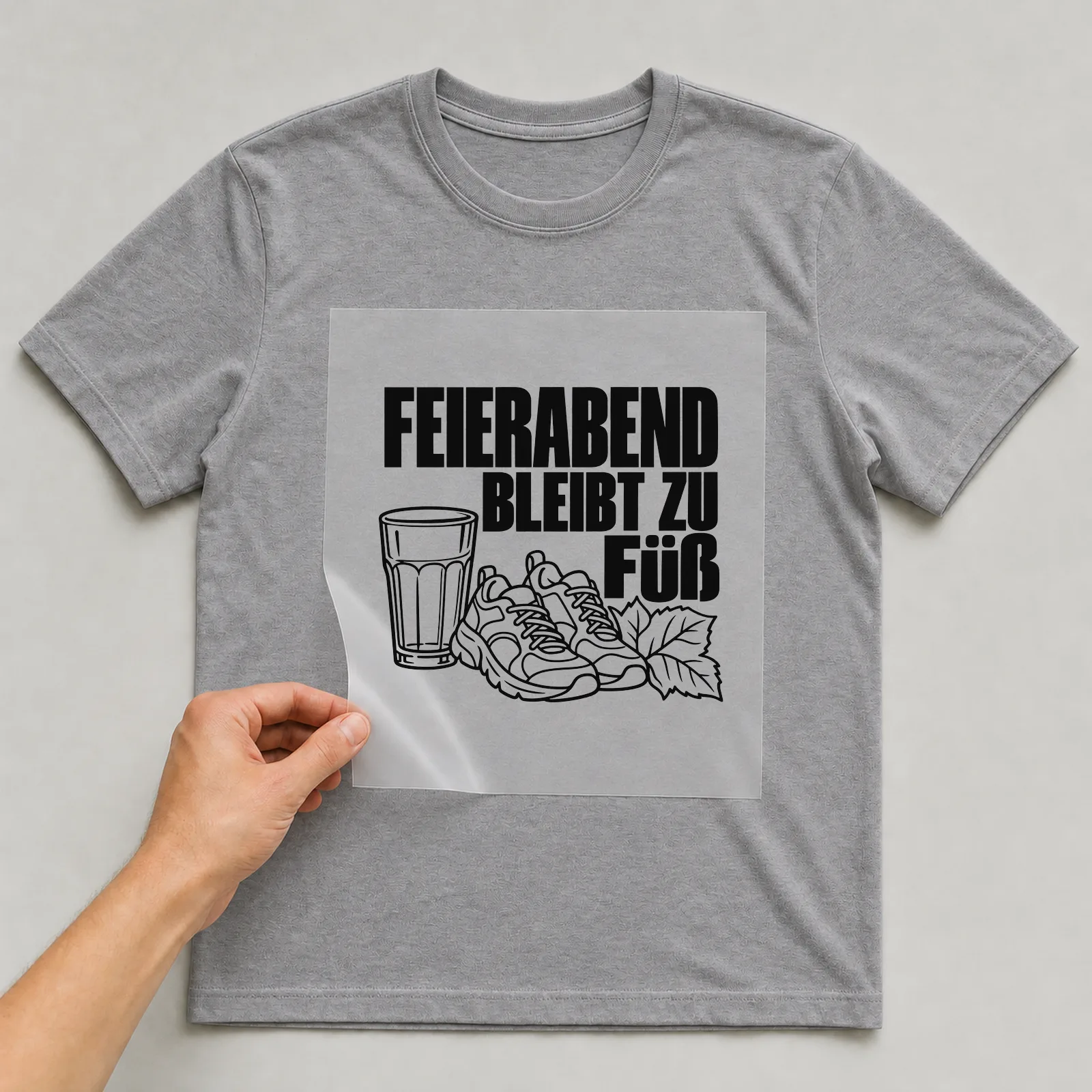 Bügelbild „FEIERABEND BLEIBT ZU FUß“ auf grauem T-Shirt, Folie wird aufgelegt