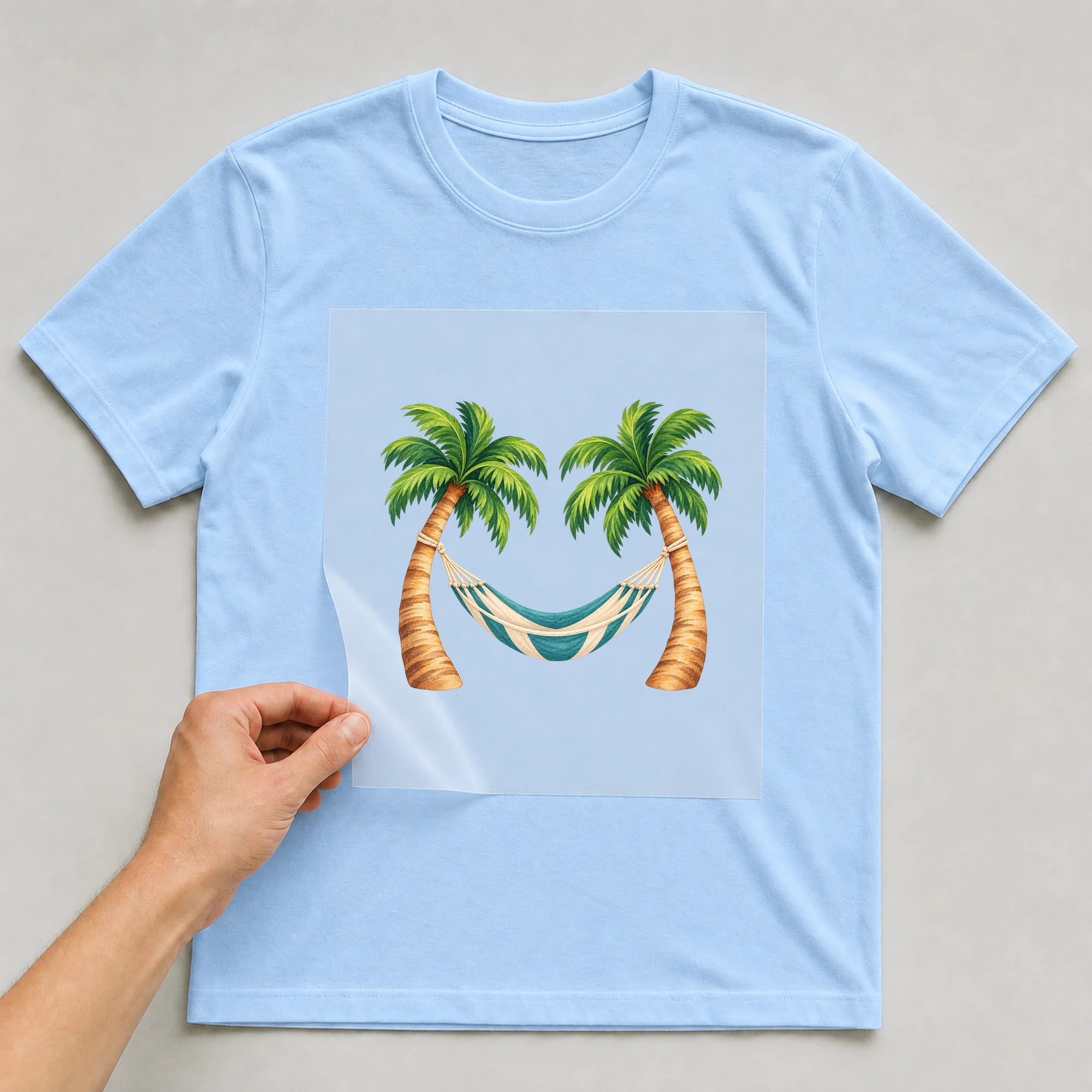Bügelbild „Urlaub Hängematte“ auf babyblauem T-Shirt, Folie wird aufgelegt
