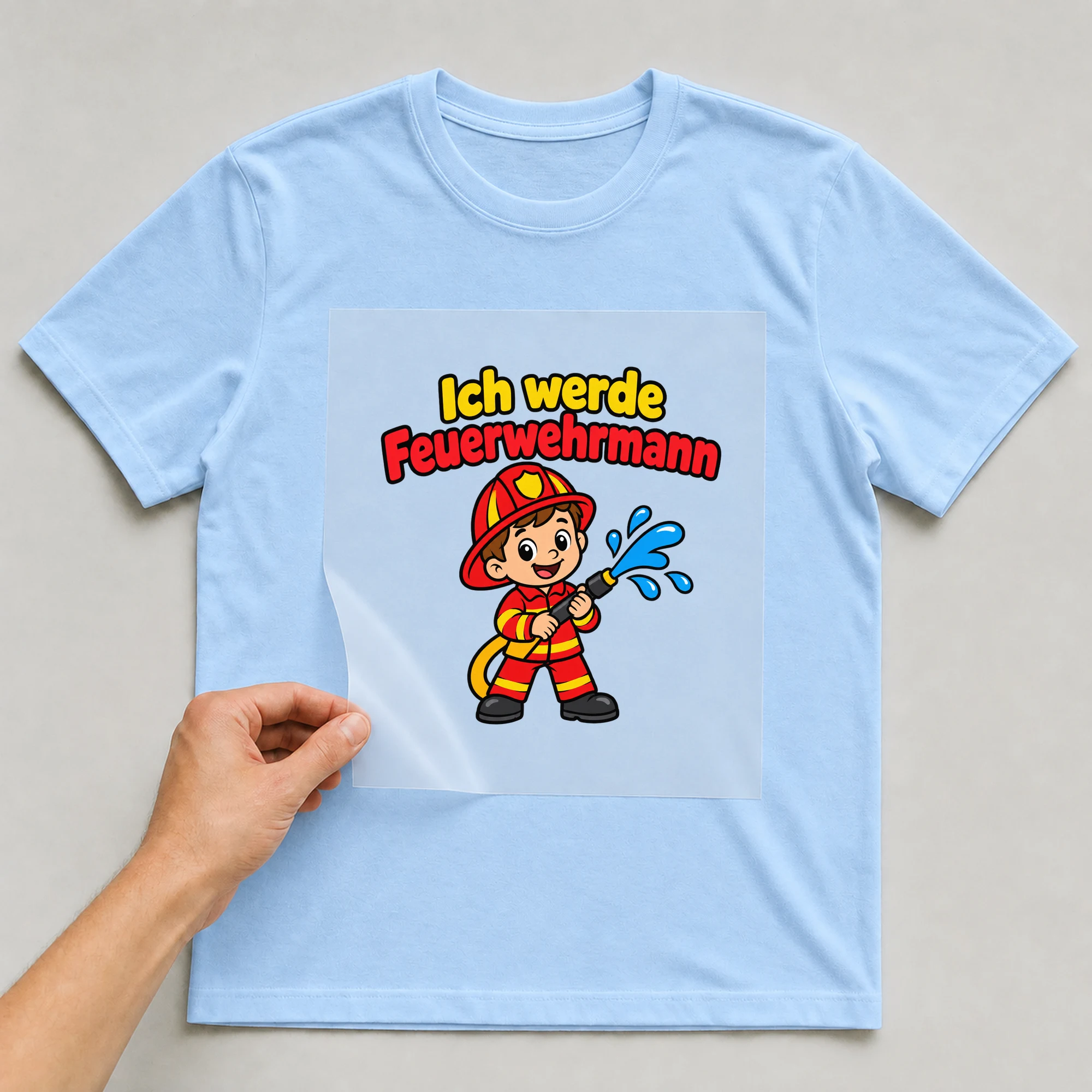 Bügelbild „Ich werde Feuerwehrmann“ auf babyblauem T-Shirt, Folie wird aufgelegt