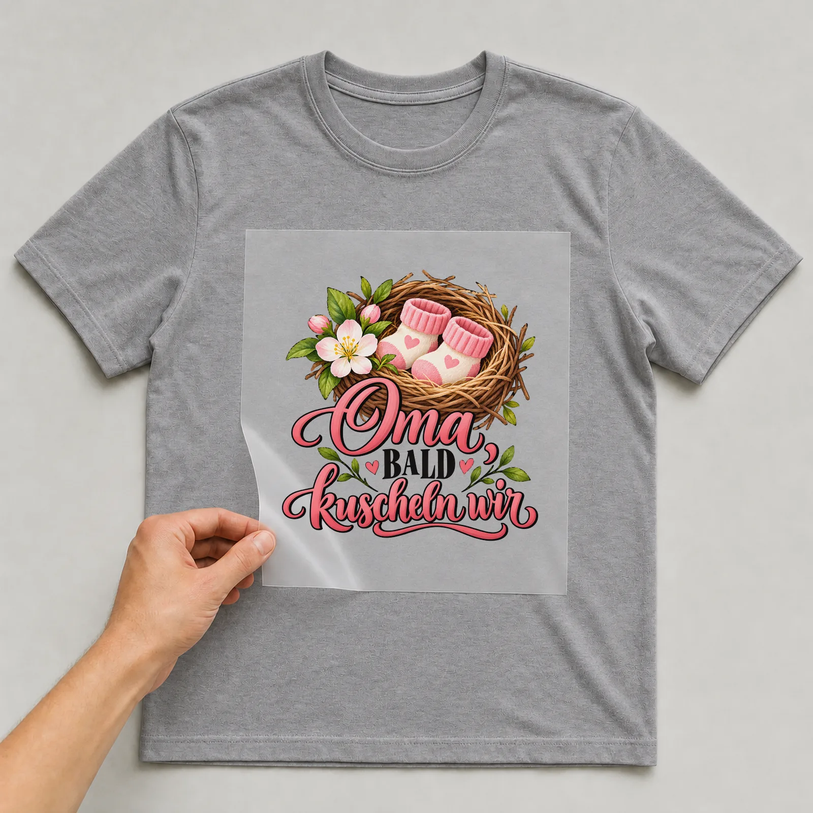 Bügelbild „Oma, bald kuscheln wir“ auf grauem T-Shirt, Folie wird aufgelegt