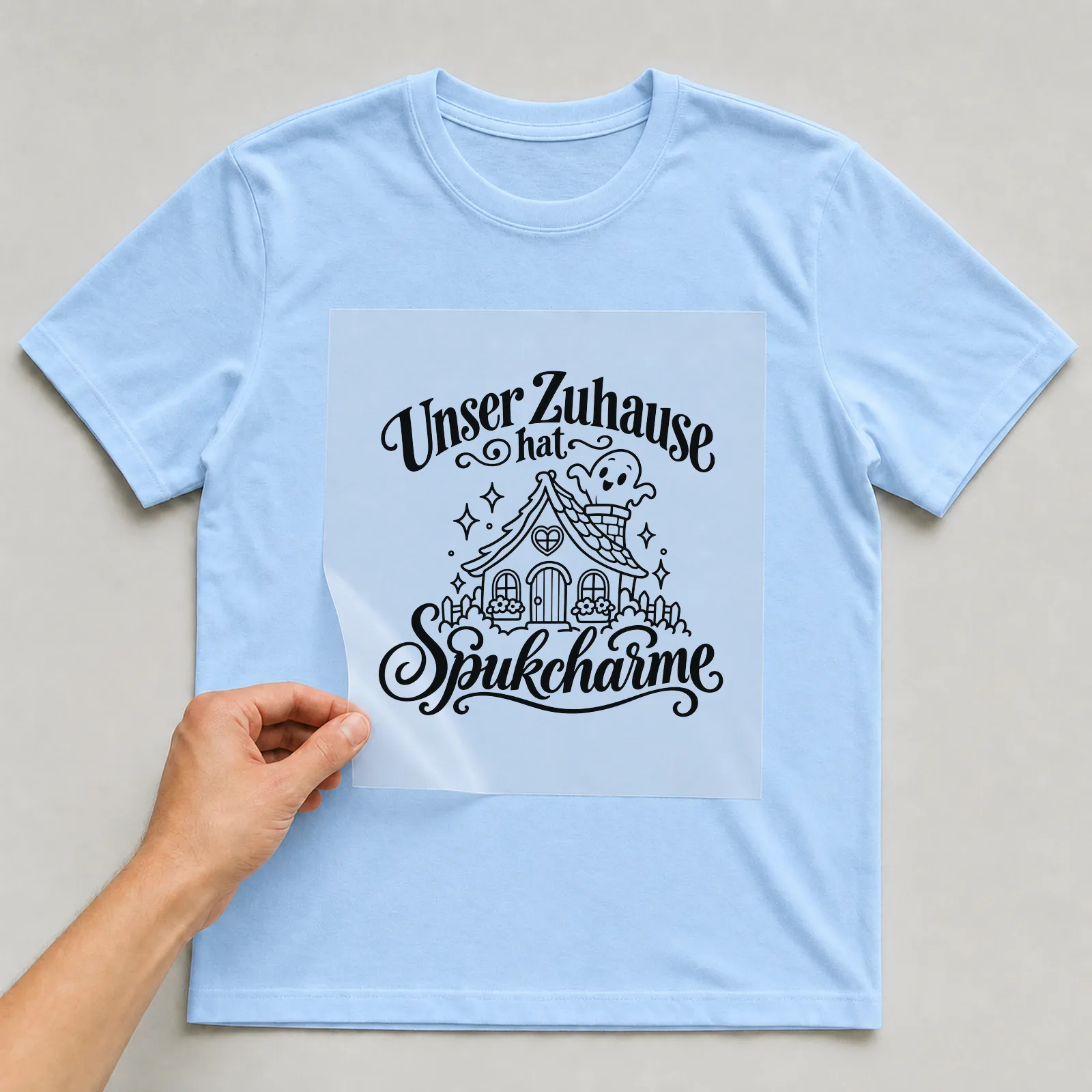Bügelbild „Unser Zuhause hat Spukcharme“ auf hellblauem T-Shirt, Folie wird aufgelegt