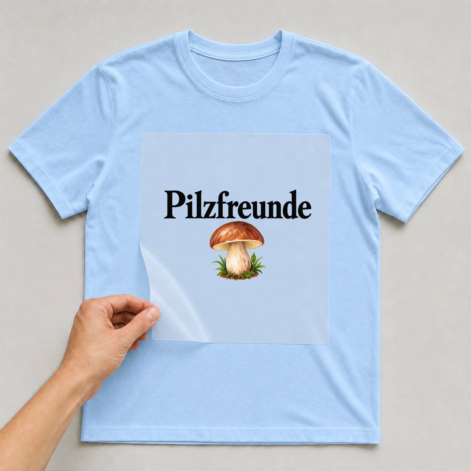 Bügelbild „Pilzfreunde“ auf babyblauem T-Shirt, Folie wird aufgelegt