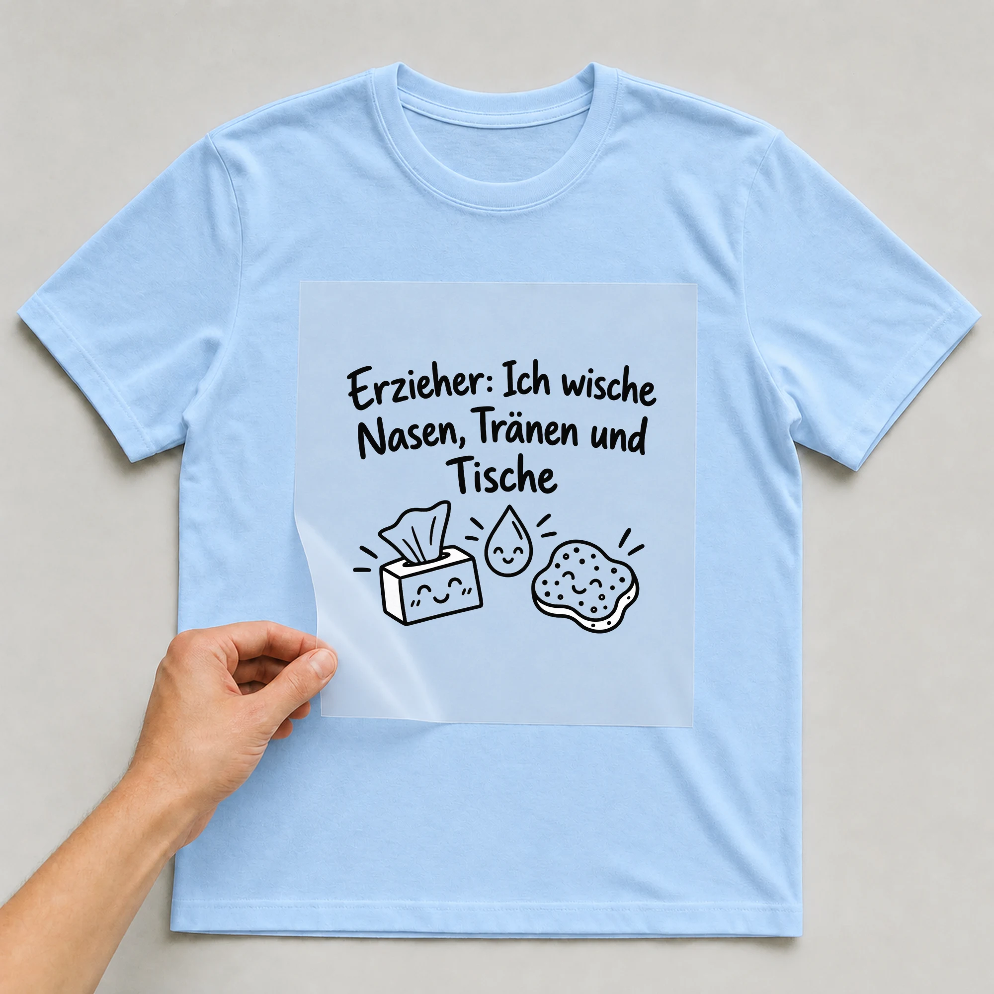Bügelbild „Erzieher: Ich wische Nasen, Tränen und Tische“ auf babyblauem T-Shirt, Folie wird aufgelegt
