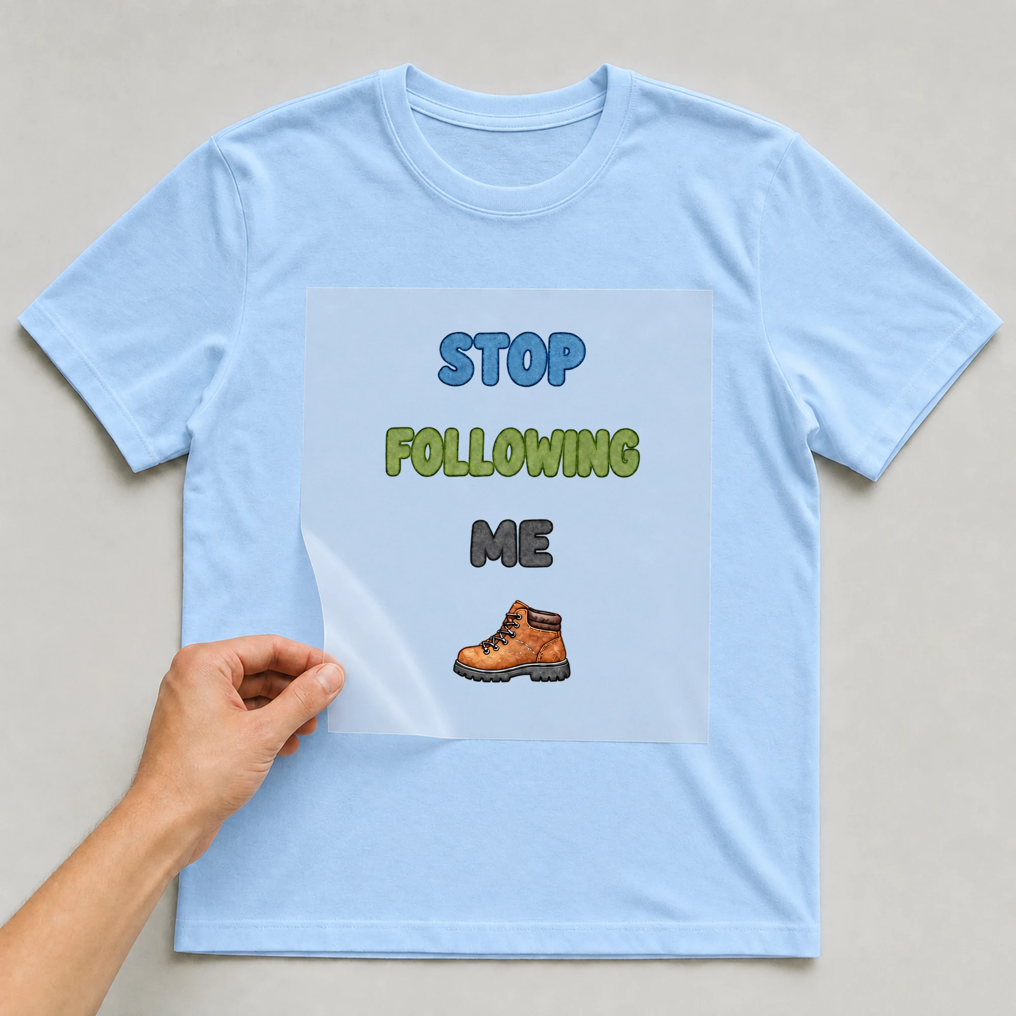 Bügelbild „STOP FOLLOWING ME“ auf babyblauem T-Shirt, Folie wird aufgelegt