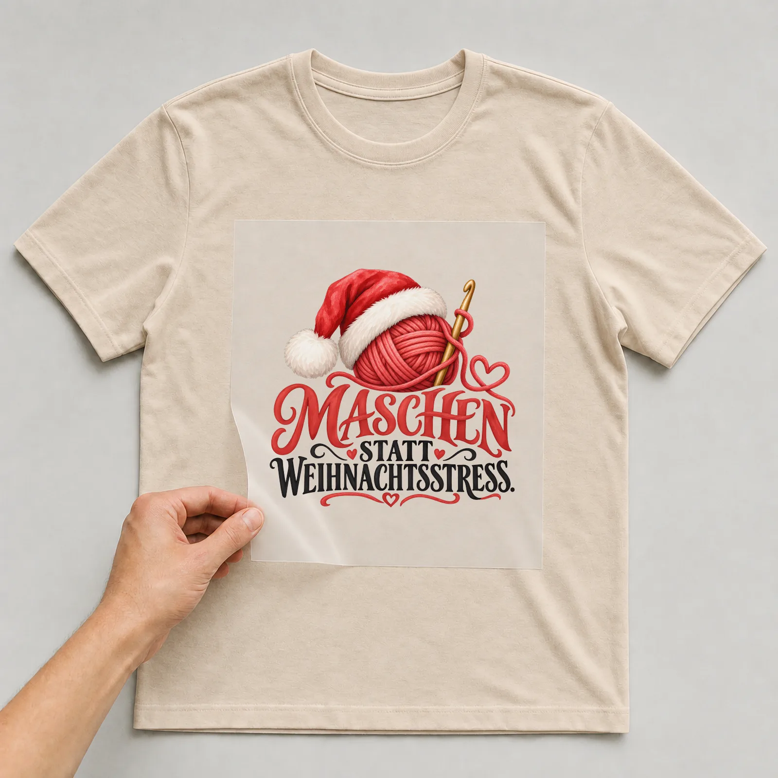 Bügelbild „Maschen statt Weihnachtsstress“ auf beigem T-Shirt, Folie wird aufgelegt