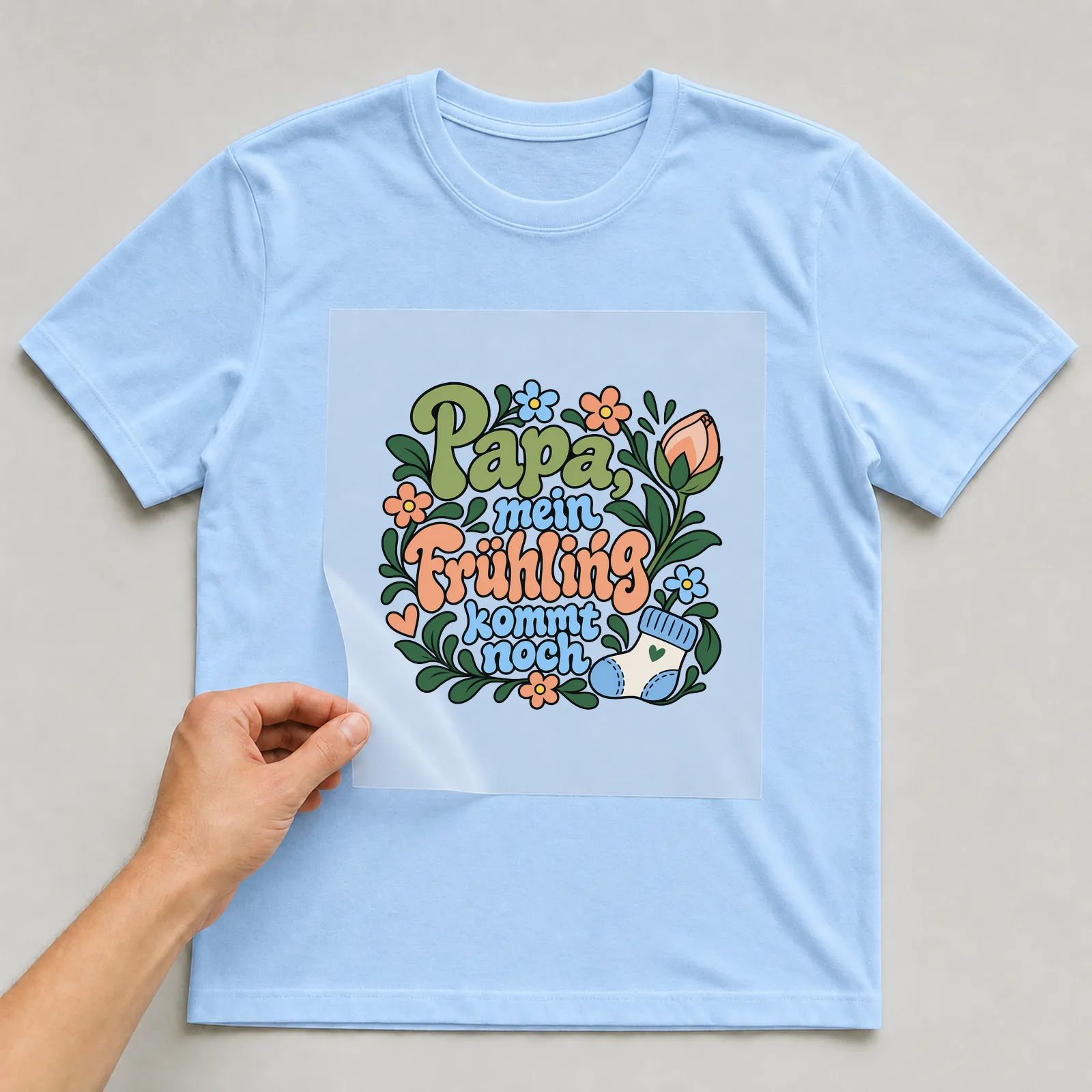 Bügelbild „Papa, mein Frühling kommt noch“ auf hellblauem T-Shirt, Folie wird aufgelegt