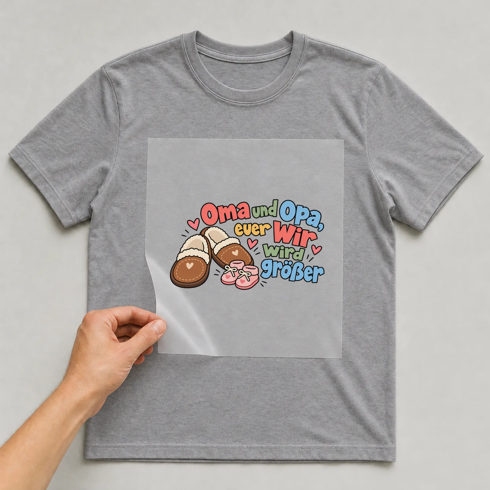 Bügelbild „Oma und Opa, euer Wir wird größer“ auf grauem T-Shirt, Folie wird aufgelegt