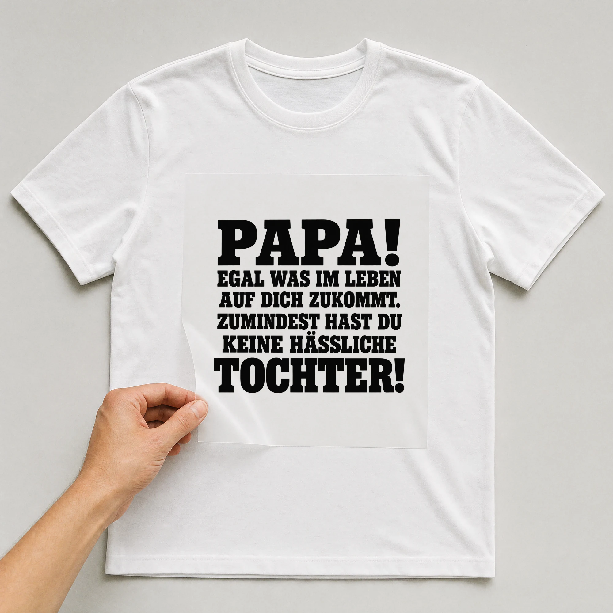 Bügelbild „Papa! Egal was im Leben auf dich zukommt. Zumindest hast du keine hässliche“ auf weißem T-Shirt, Folie wird aufgelegt