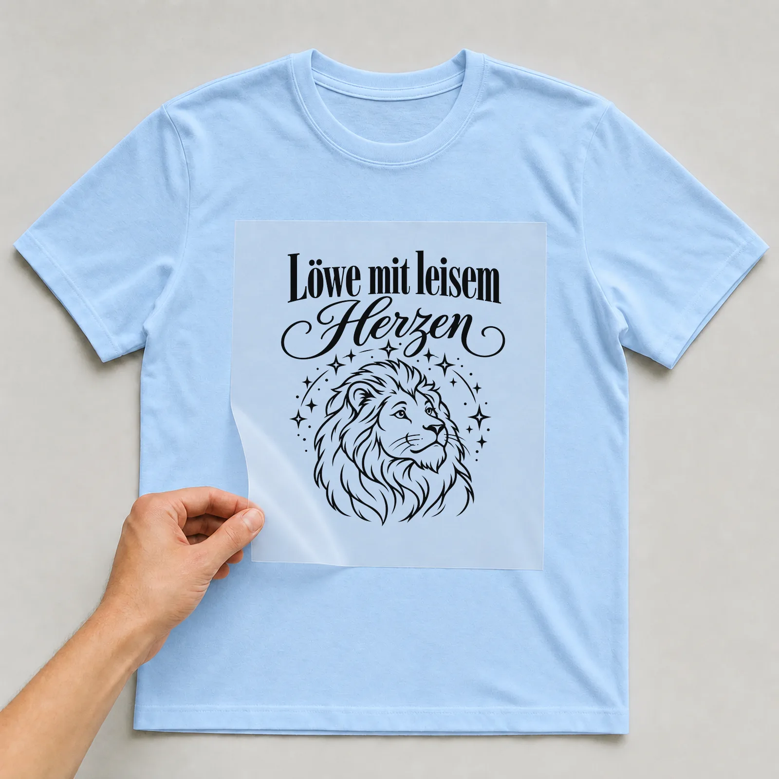 Bügelbild „Löwe mit leisem Herzen“ auf hellblauem T-Shirt, Folie wird aufgelegt