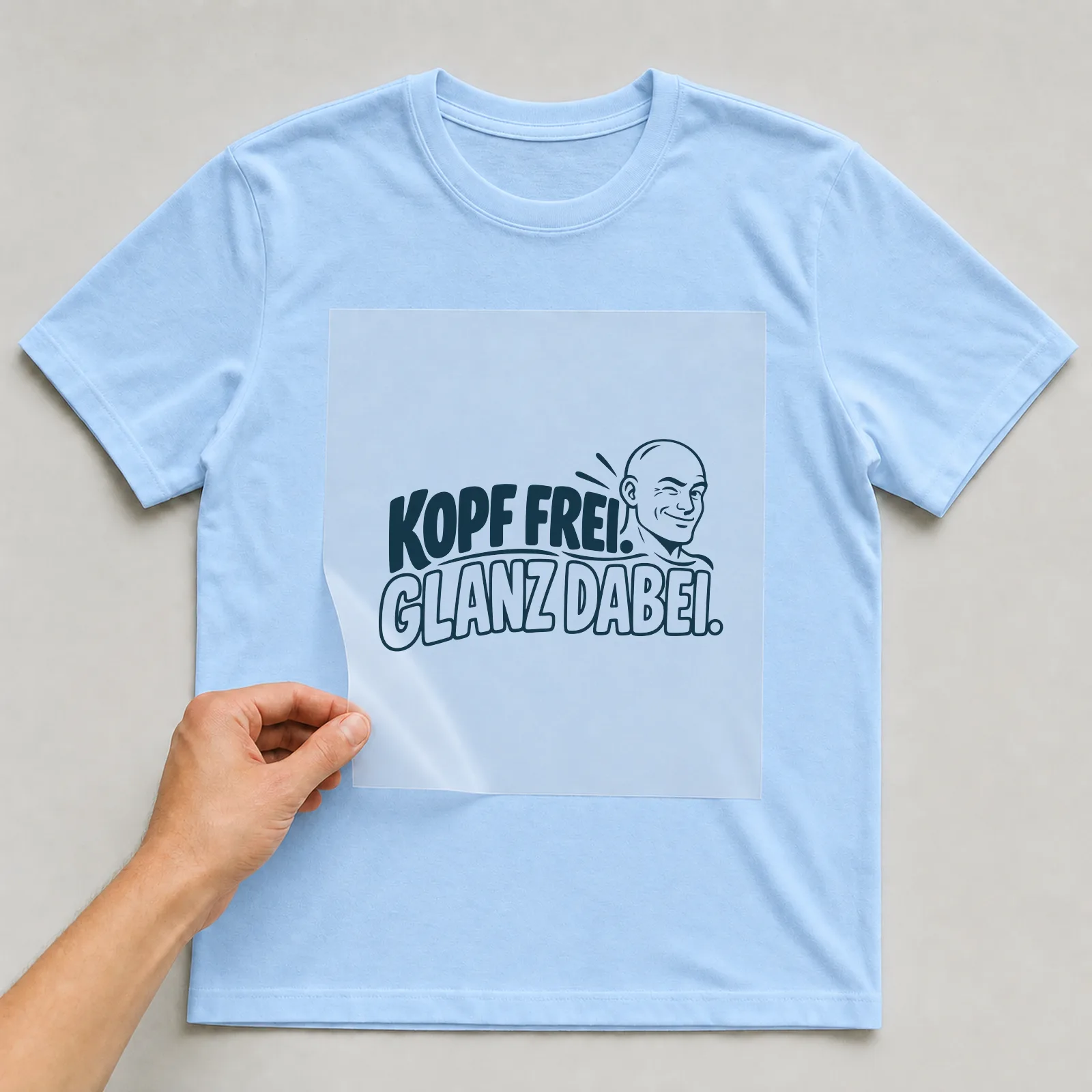 Bügelbild „Kopf frei. Glanz dabei.“ auf hellblauem T-Shirt, Folie wird aufgelegt