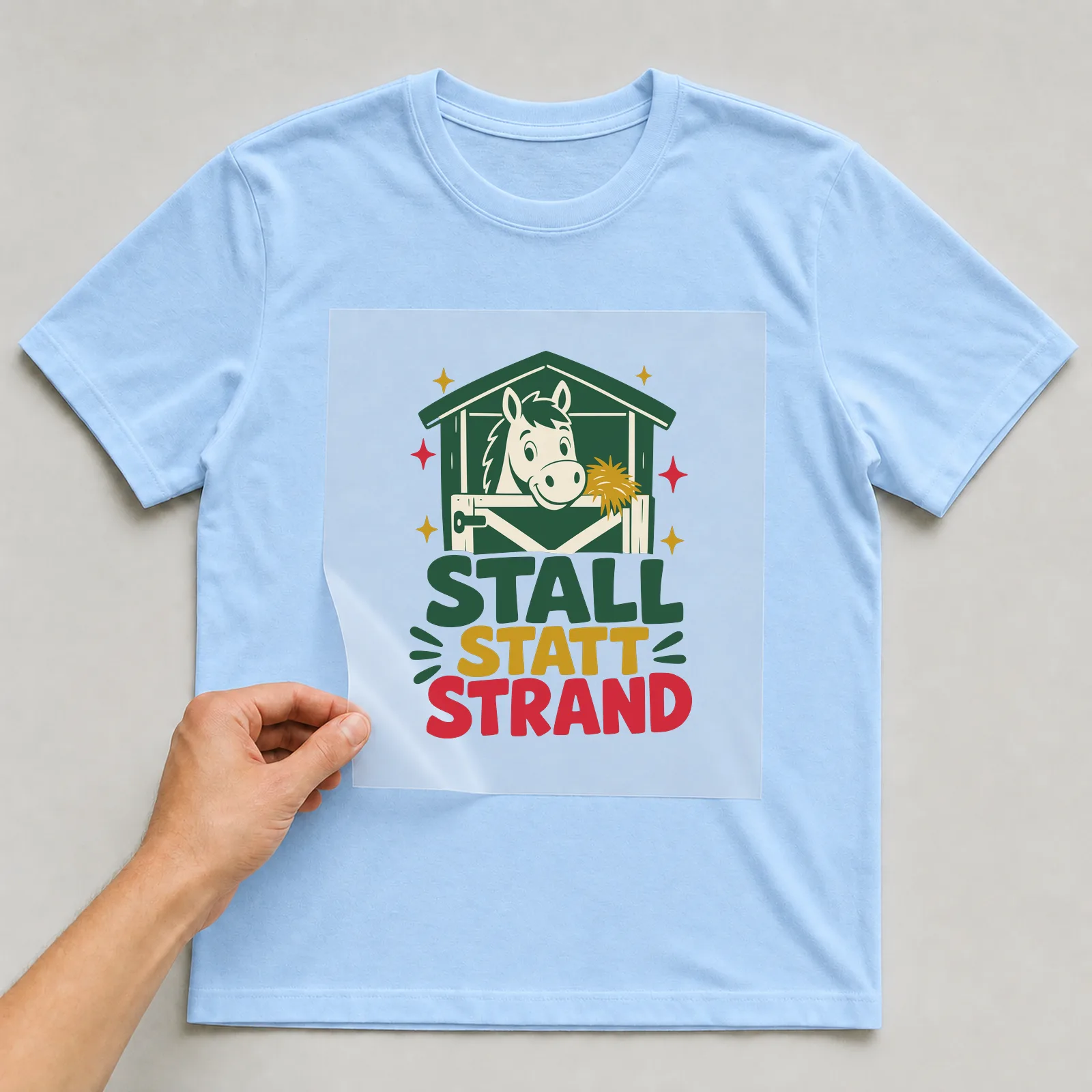 Bügelbild Stall statt Strand auf hellblauem T-Shirt, Folie wird aufgelegt