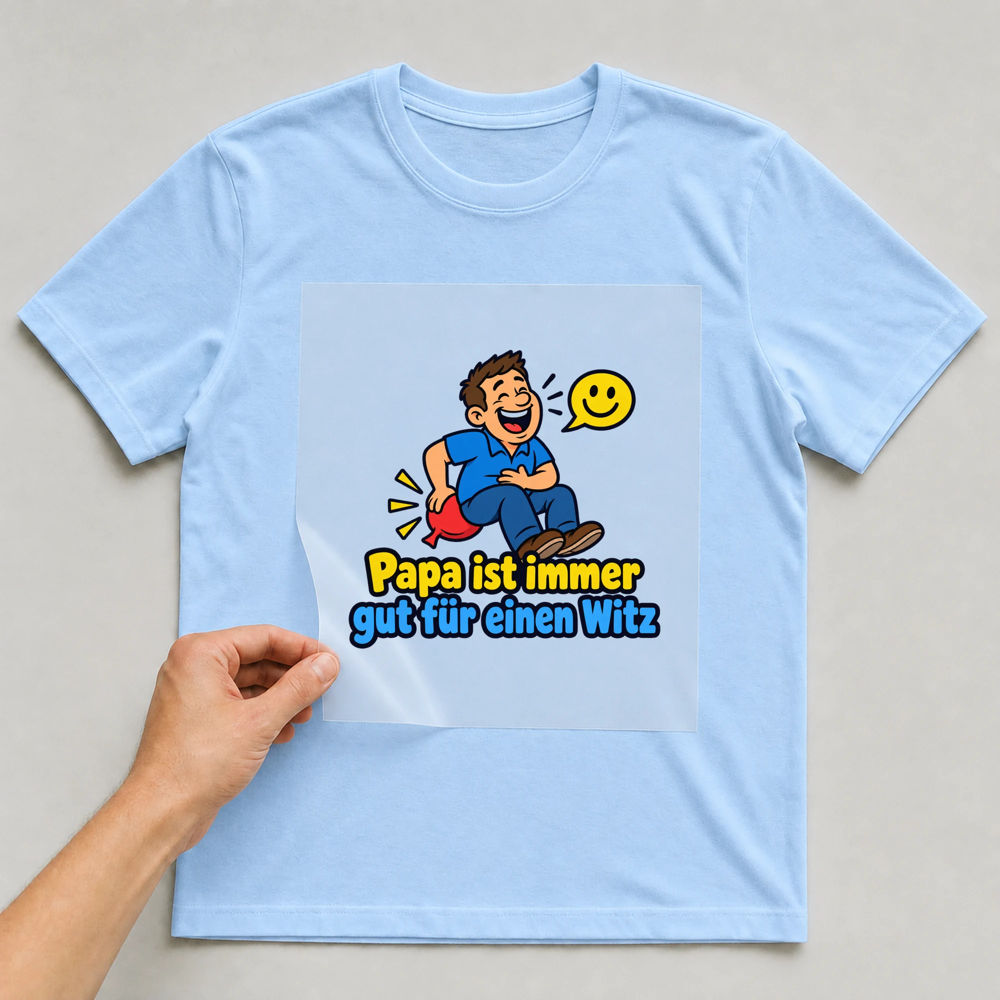 Bügelbild „Papa ist immer gut für einen Witz“ auf babyblauem T-Shirt, Folie wird aufgelegt