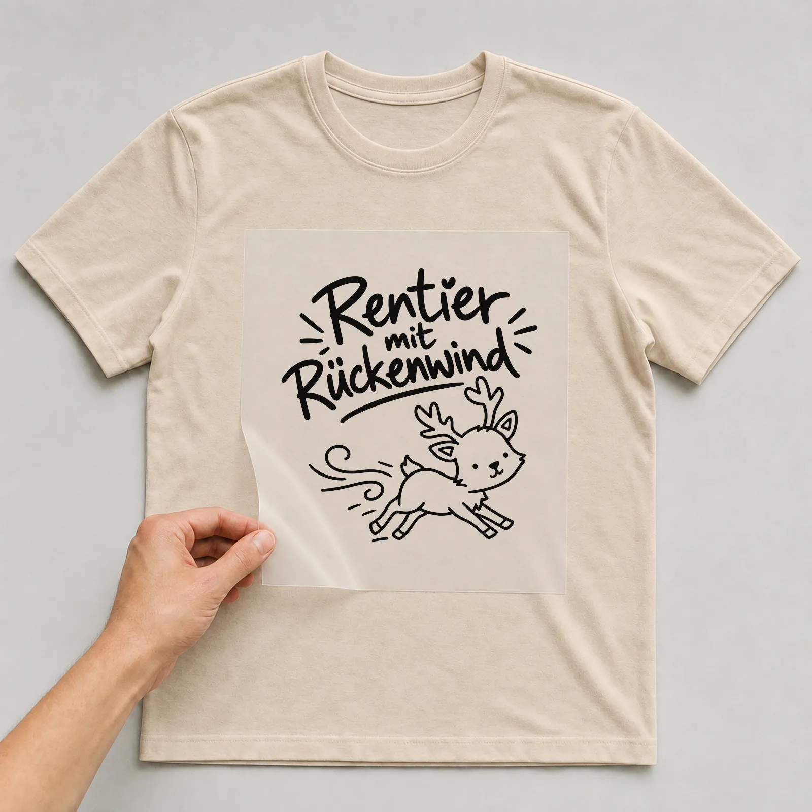 Bügelbild „Rentier mit Rückenwind“ auf beigem T-Shirt, Folie wird aufgelegt