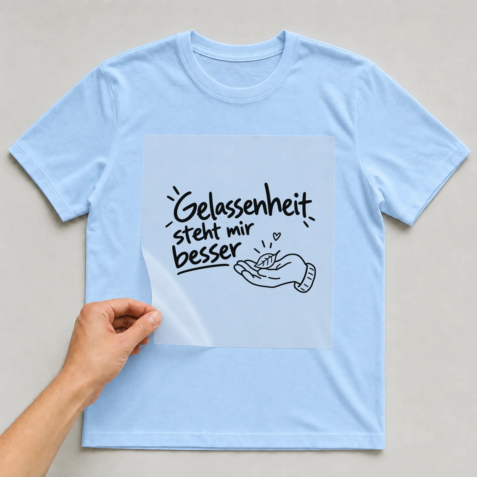 Bügelbild „Gelassenheit steht mir besser“ auf hellblauem T-Shirt, Folie wird aufgelegt