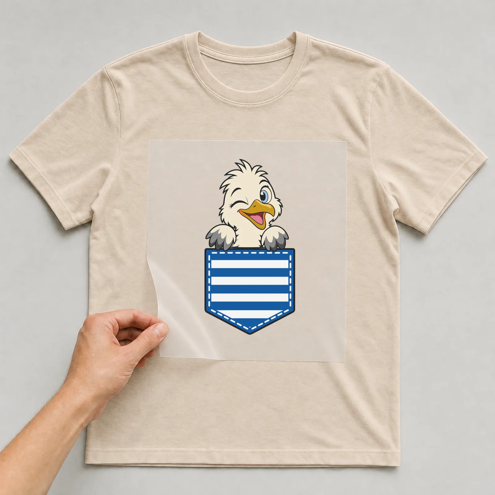 Bügelbild Brusttasche Möwe zwinkernd auf beigem T-Shirt, Folie wird aufgelegt