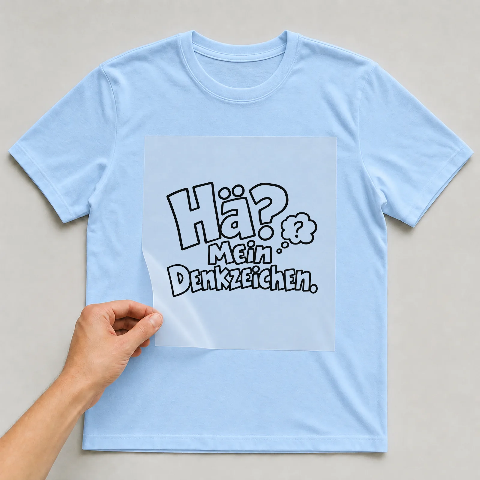 Bügelbild „Hä? Mein Denkzeichen.“ auf hellblauem T-Shirt, Folie wird aufgelegt