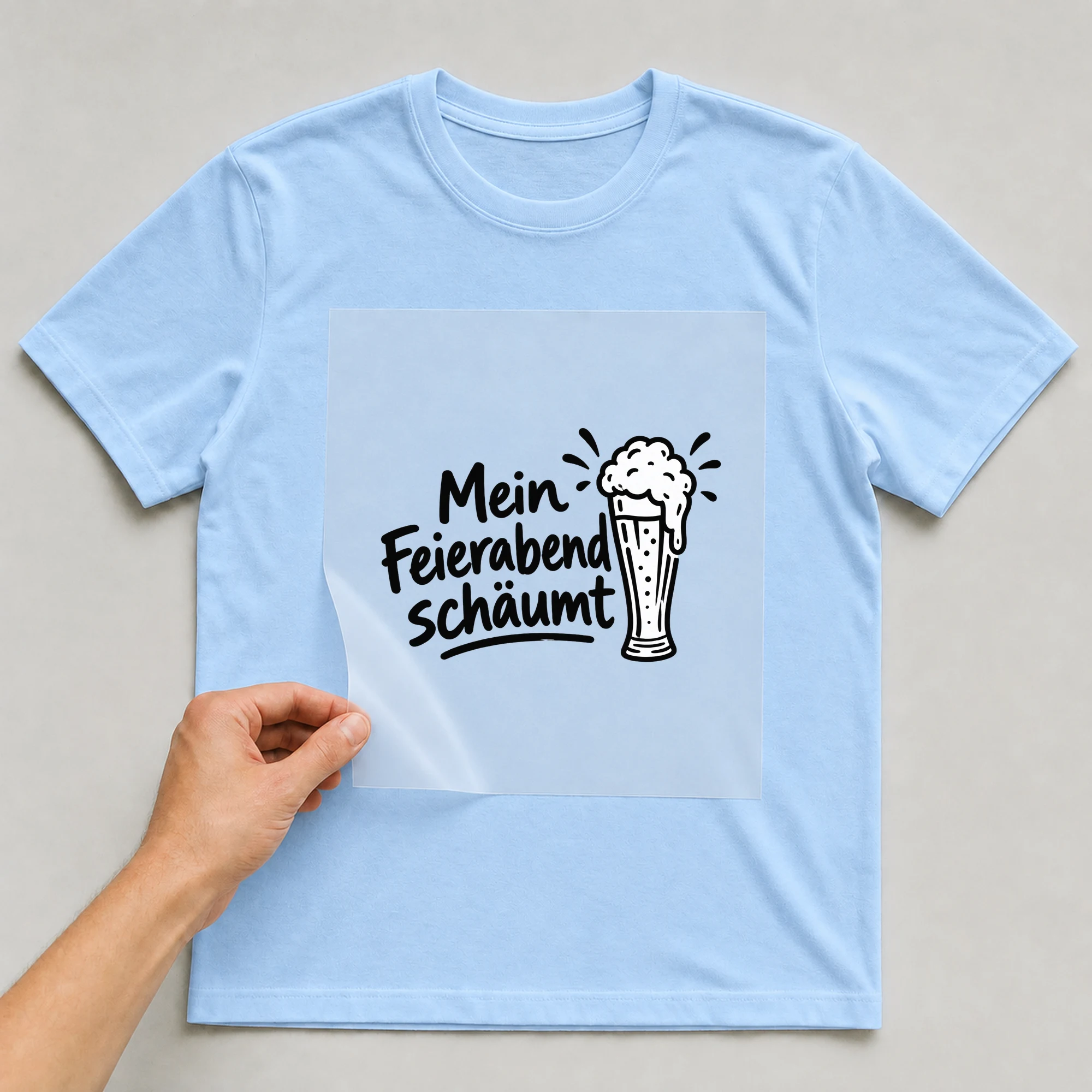 Bügelbild „Mein Feierabend schäumt“ auf babyblauem T-Shirt, Folie wird aufgelegt