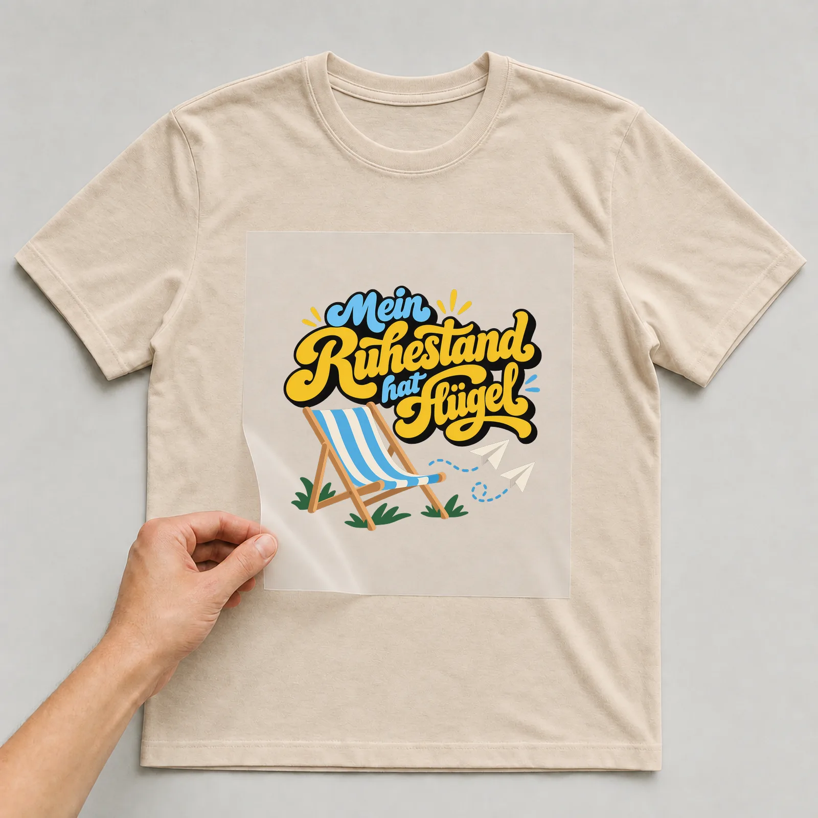 Bügelbild „Mein Ruhestand hat Flügel“ auf beigem T-Shirt, Folie wird aufgelegt