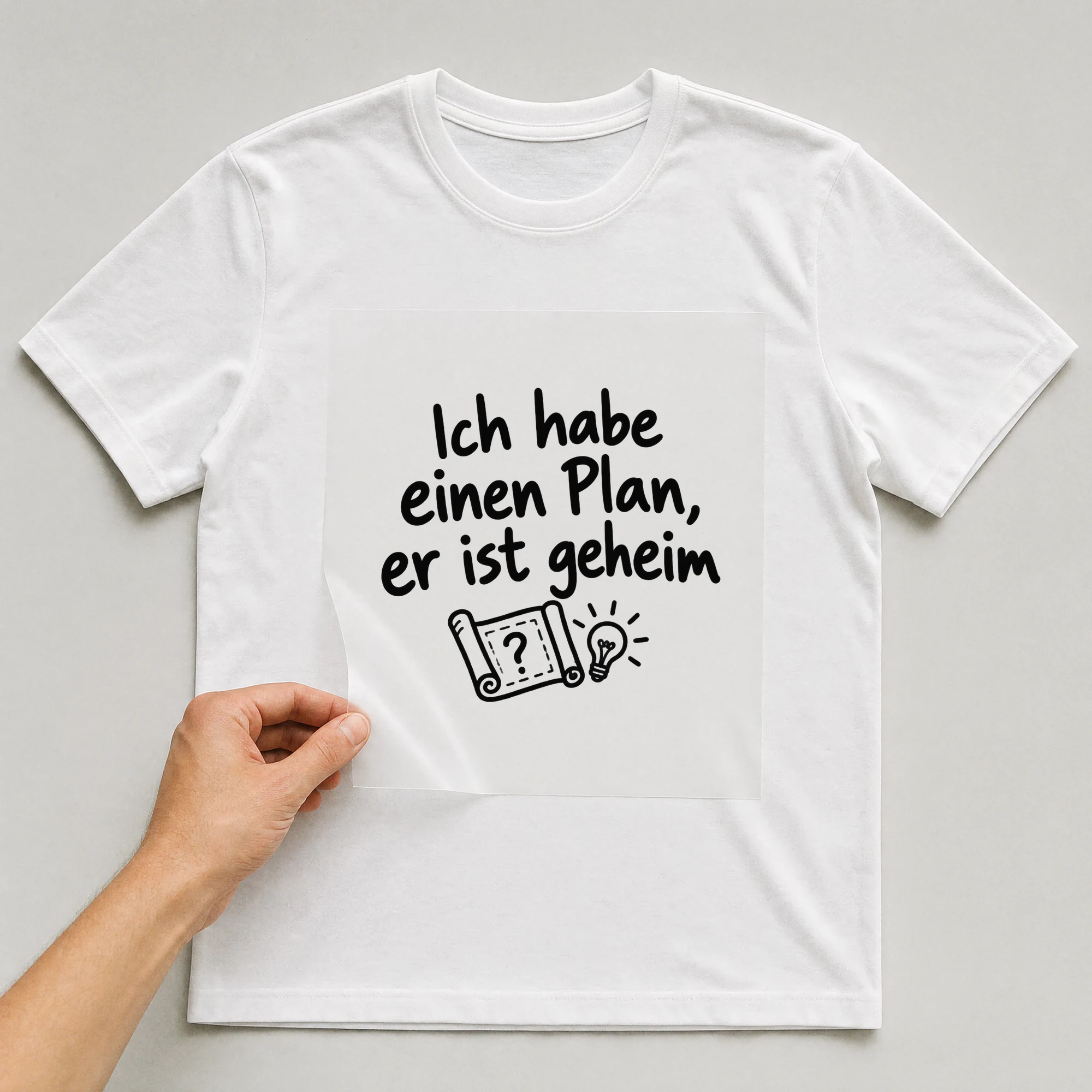Bügelbild „Ich habe einen Plan, er ist geheim“ auf weißem T-Shirt, Folie wird aufgelegt